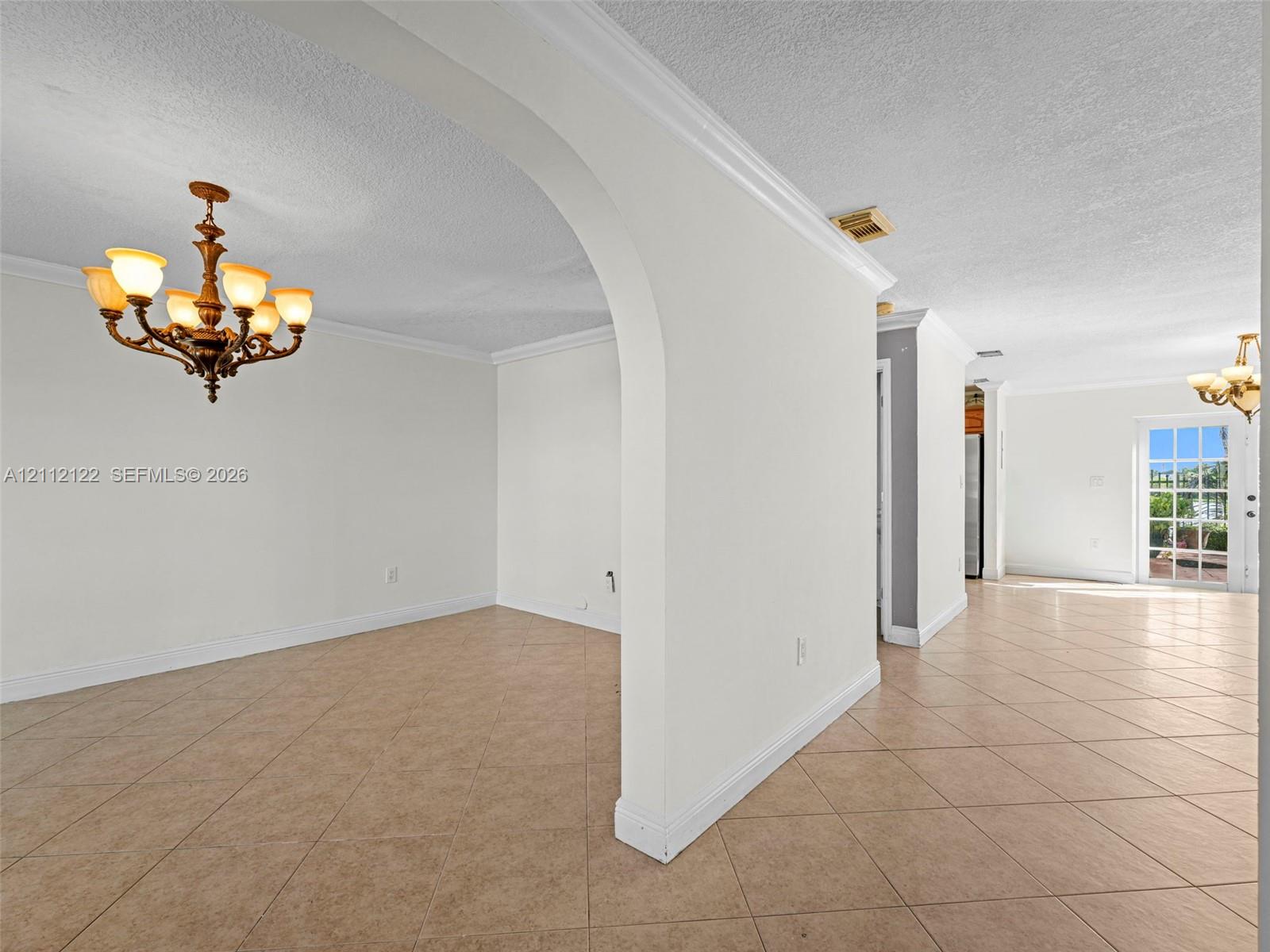 Interior space featuring a prominent arched entryway, ceramic tile flooring set on a diagonal, crown molding, and two multi-armed chandeliers
