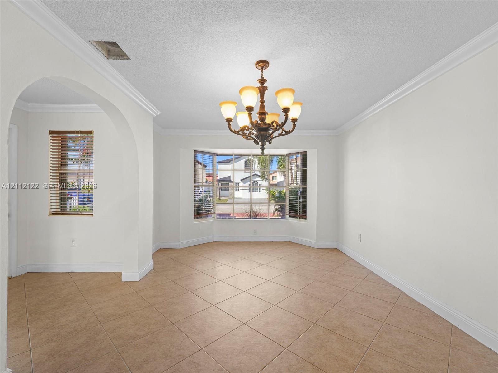 Room featuring tile flooring, crown molding, arched entry, bay window, and a multi-arm chandelier