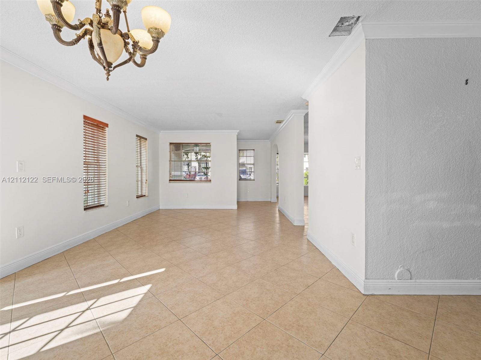 Open-concept space featuring diagonal tile flooring, crown molding, multi-light chandelier, and horizontal wood-finish blinds