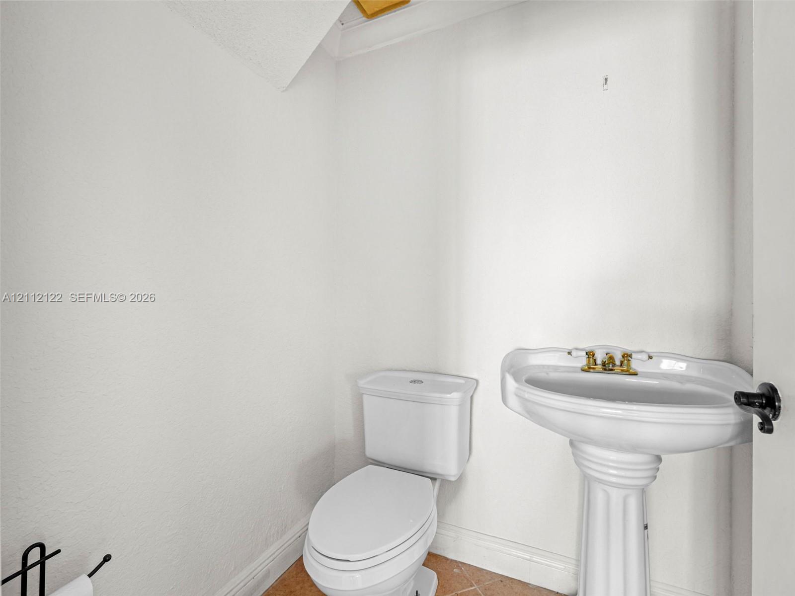 White porcelain pedestal sink with a brass-finish dual-handle faucet and a white porcelain toilet