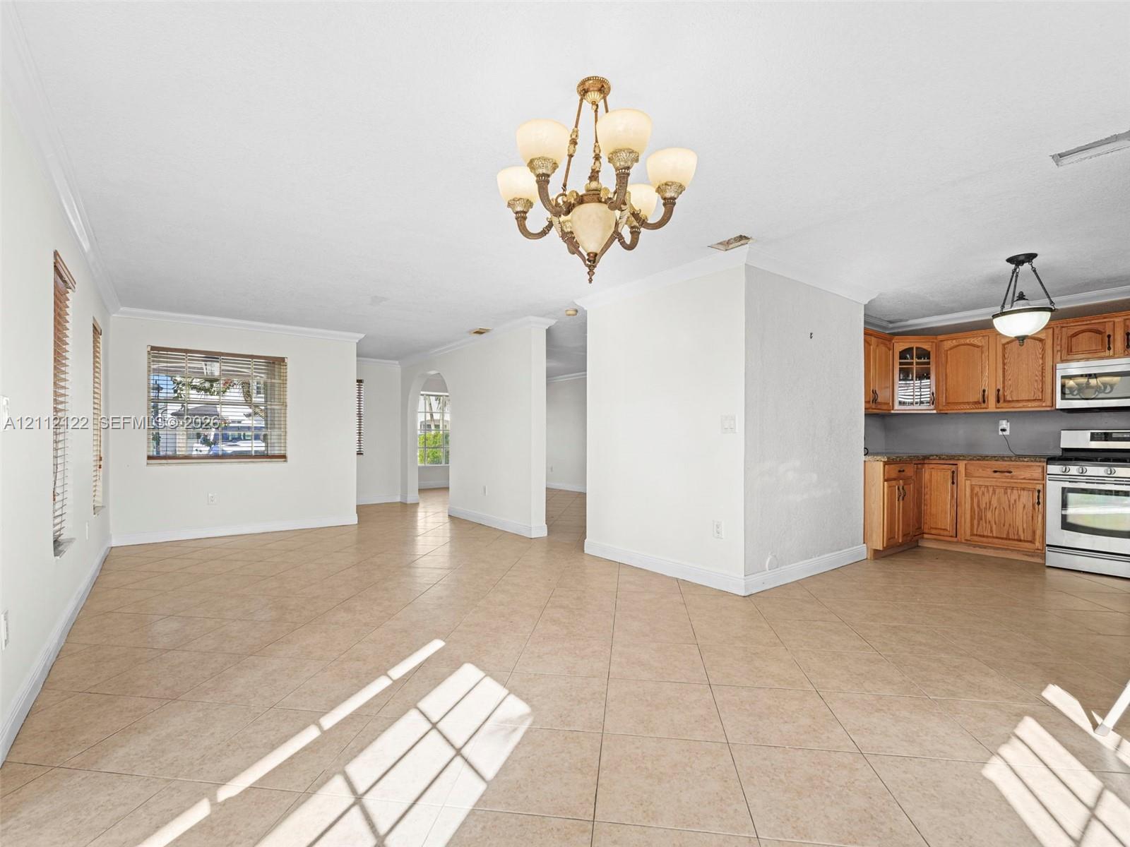 Open-concept interior featuring tile flooring, crown molding, arched entryways, a multi-arm chandelier, and built-in wood cabinetry
