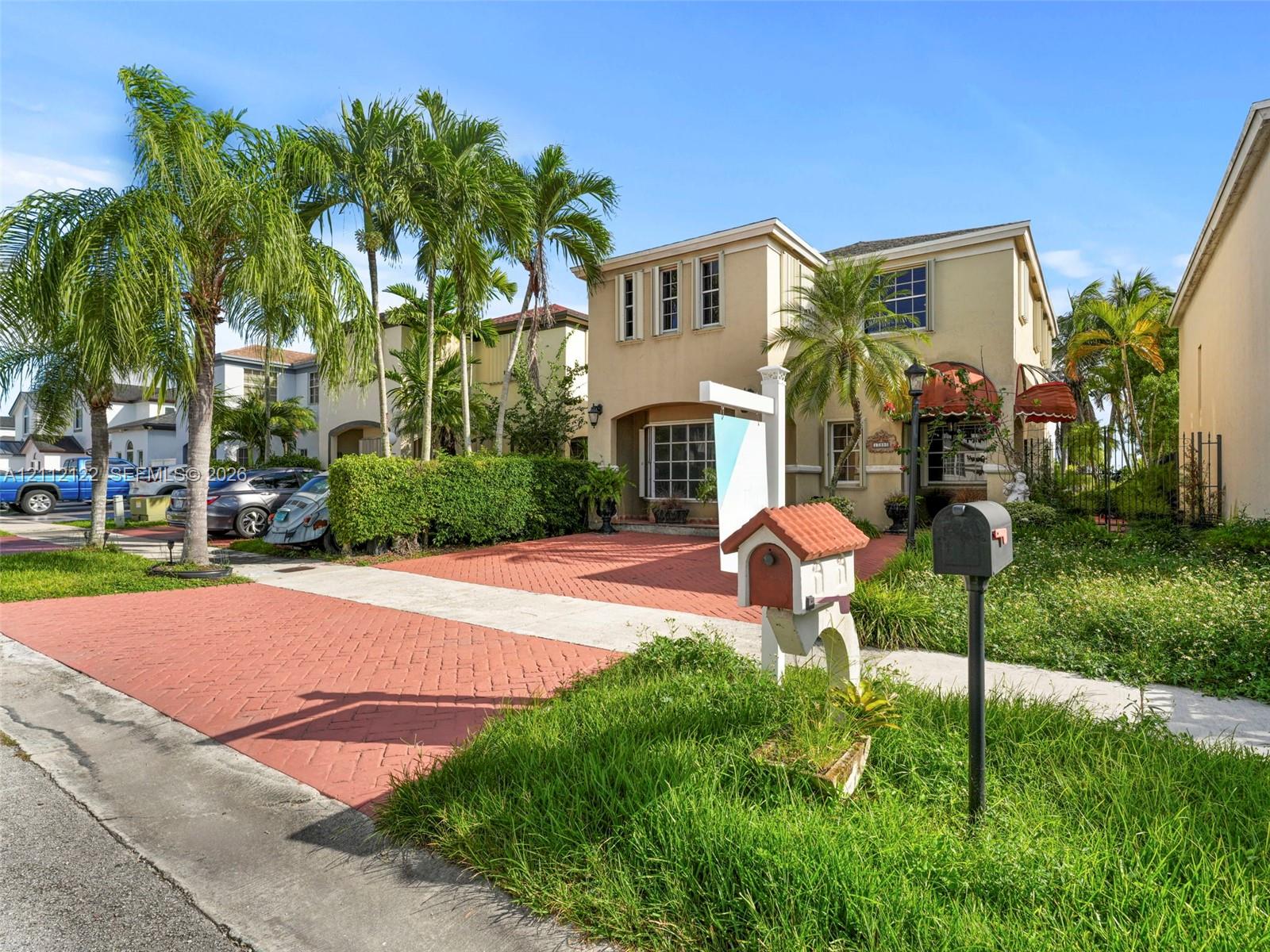 Two-story stucco exterior featuring a red brick-patterned driveway, multi-pane bay window, and custom decorative awnings