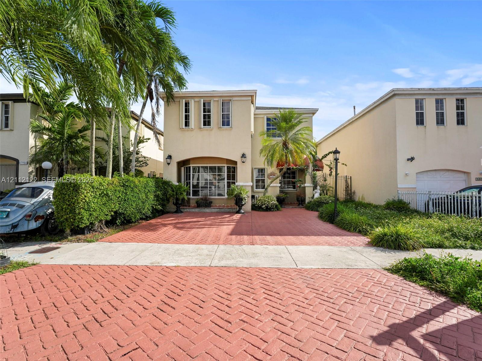 Two-story stucco exterior featuring a herringbone-patterned brick paver driveway, bay window, and manicured landscaping