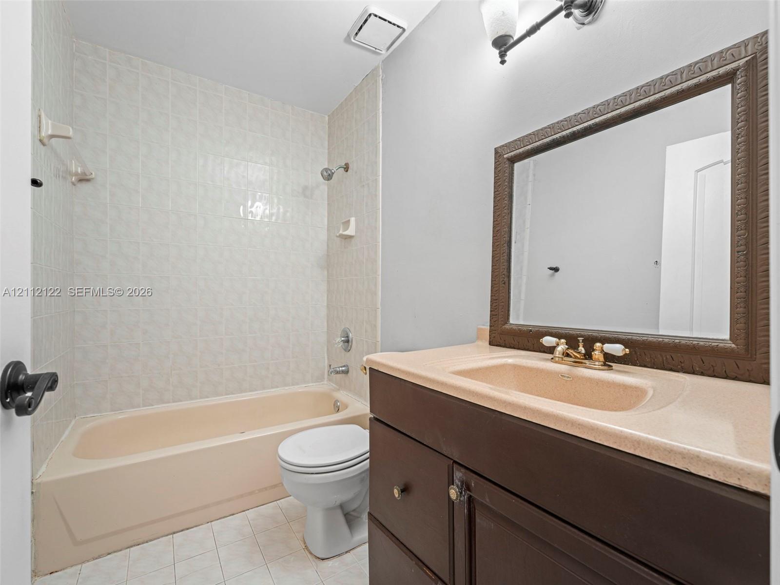 Bathroom featuring a vanity with an integrated countertop, dark wood-finish cabinetry, a framed mirror, and a tiled tub-shower enclosure