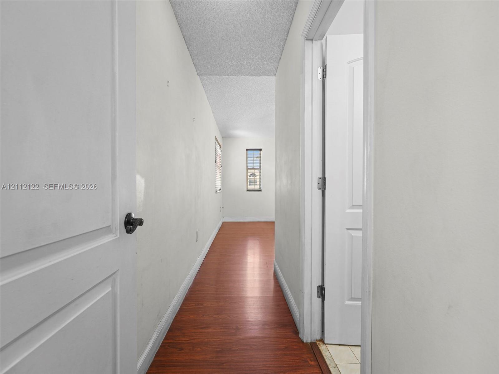 Hallway featuring wood-finish flooring, white walls, and interior paneled doors with matte black hardware