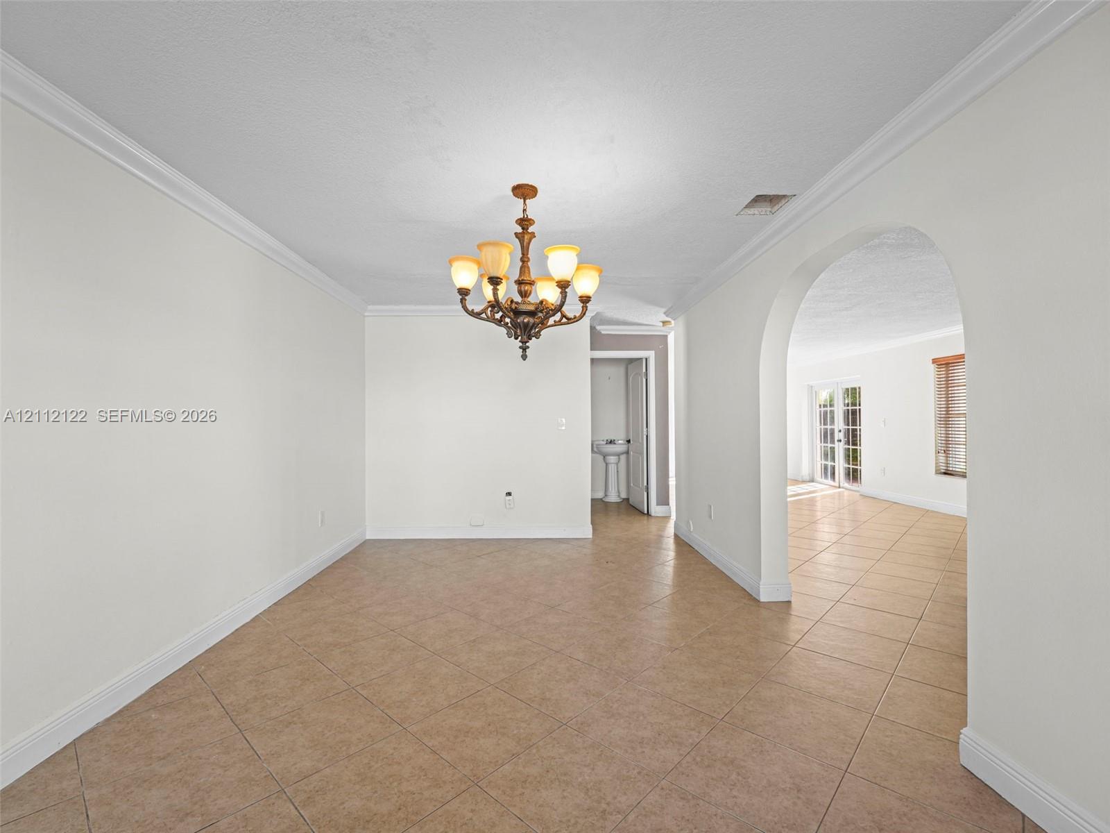 Interior space featuring neutral wall paint, tile flooring, crown molding, an arched passage, and a decorative multi-arm chandelier