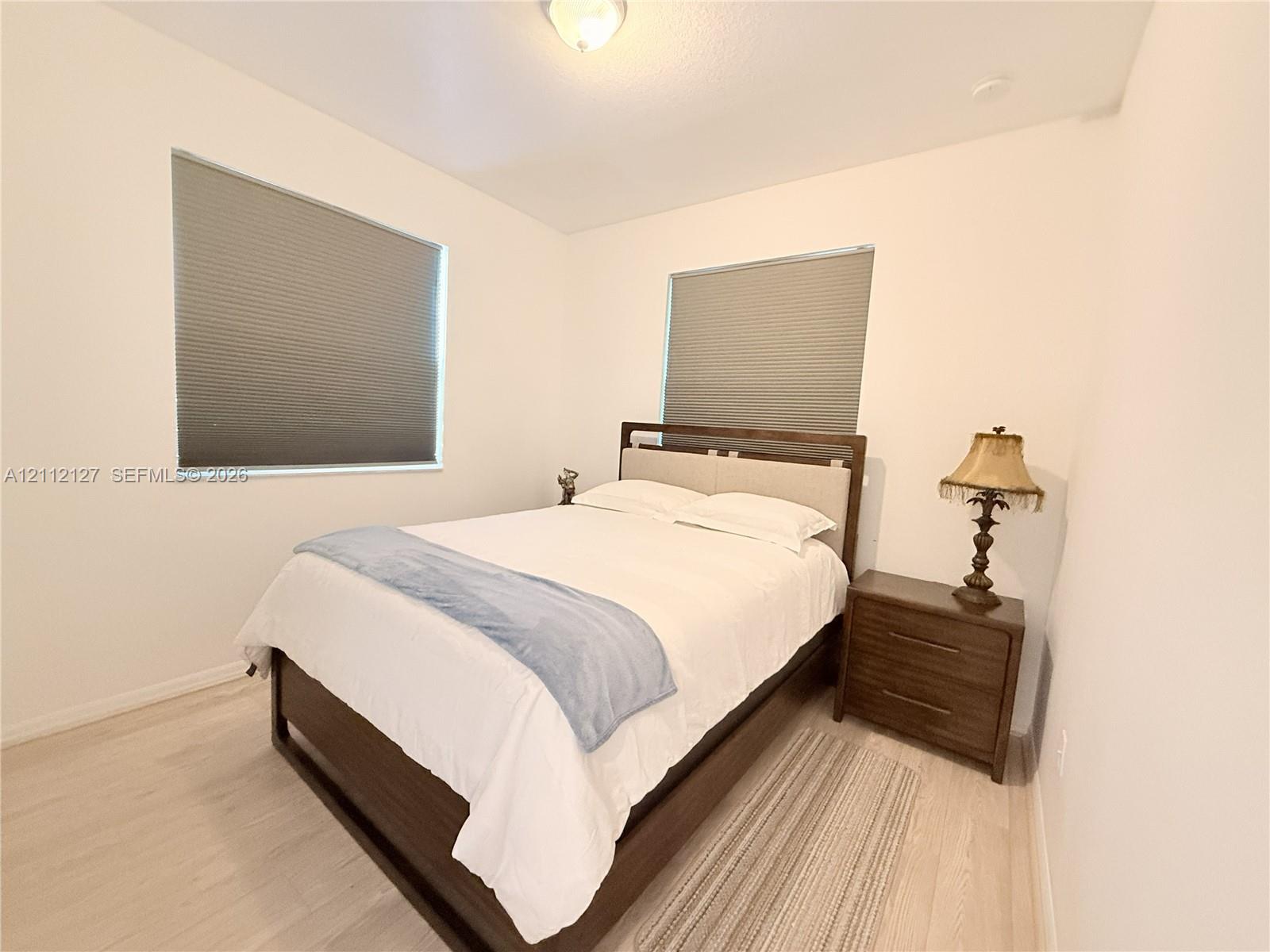 Neutral walls, light-toned wood-finish flooring, dual windows with fitted cellular shades, and a central ceiling-mounted light fixture