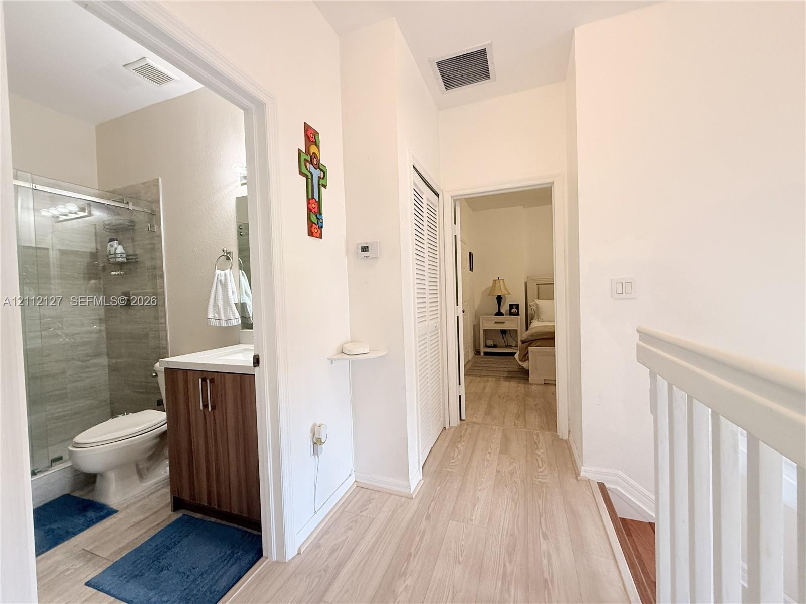 Bathroom featuring a glass-enclosed shower with tiled surround, wood-finish vanity cabinet, and wood-finish flooring