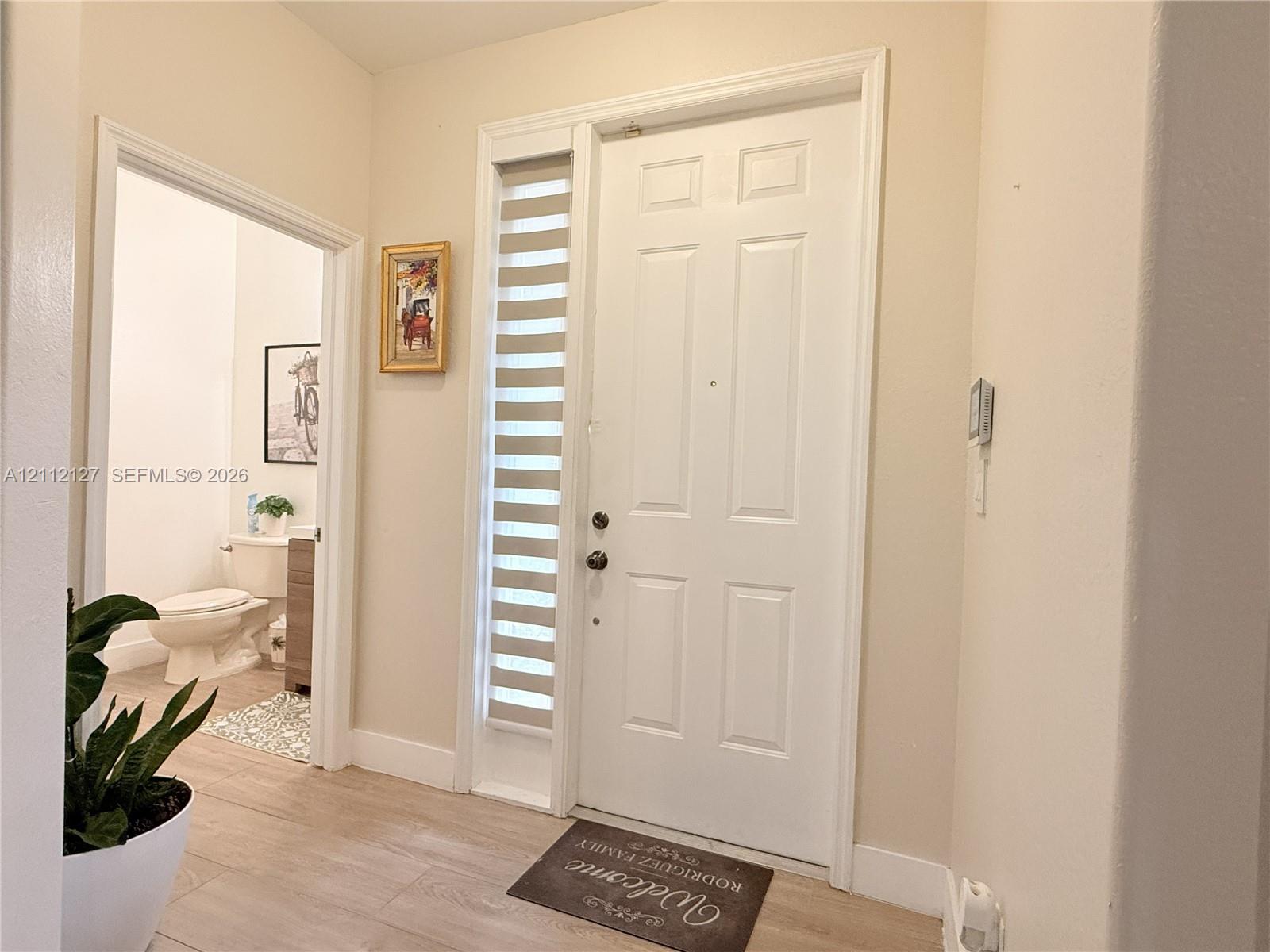 Entryway featuring a six-panel white door with vertical sidelight window and wood-finish flooring