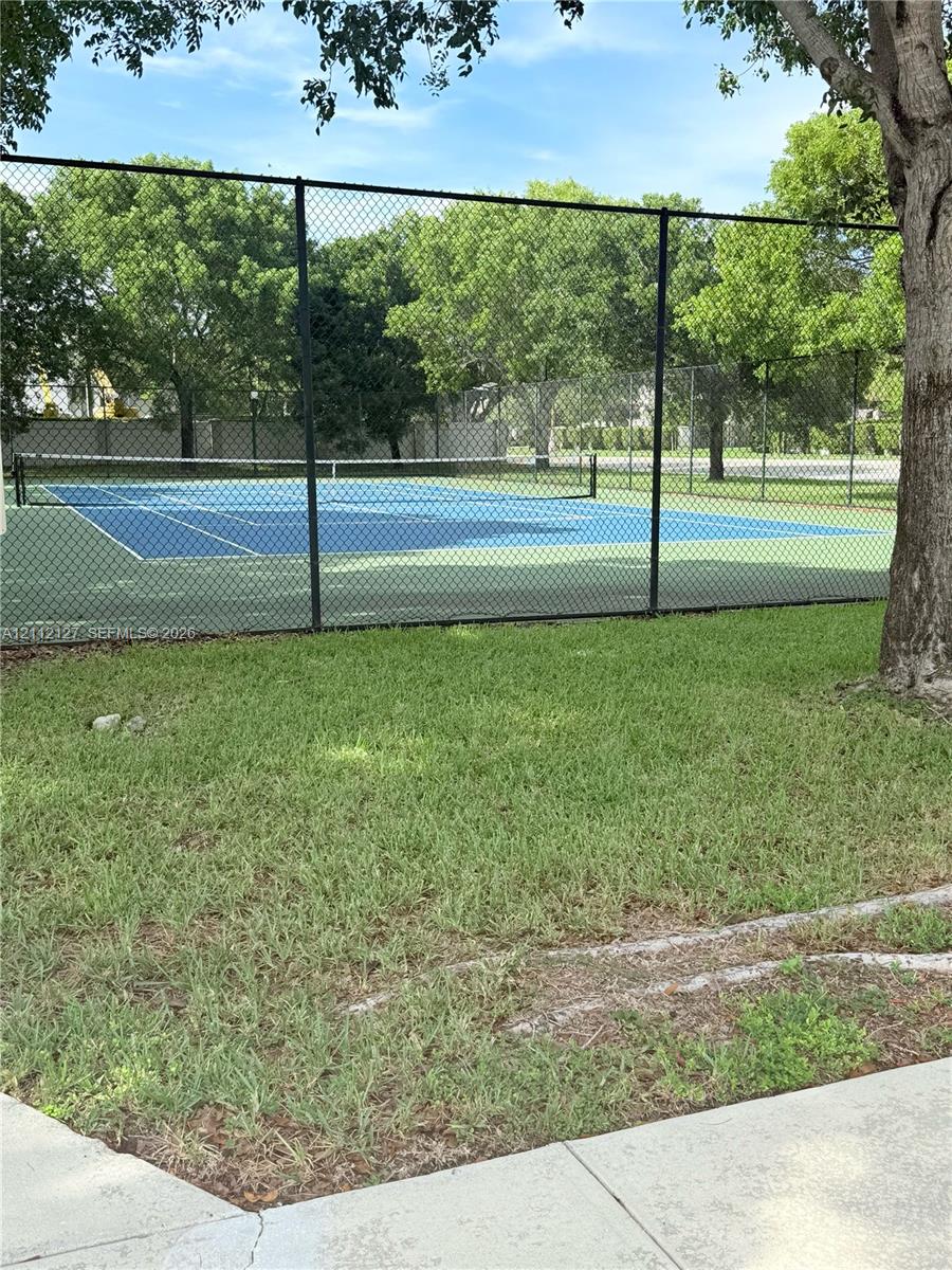 Private tennis court featuring a blue surface, mesh fencing, and a permanent net