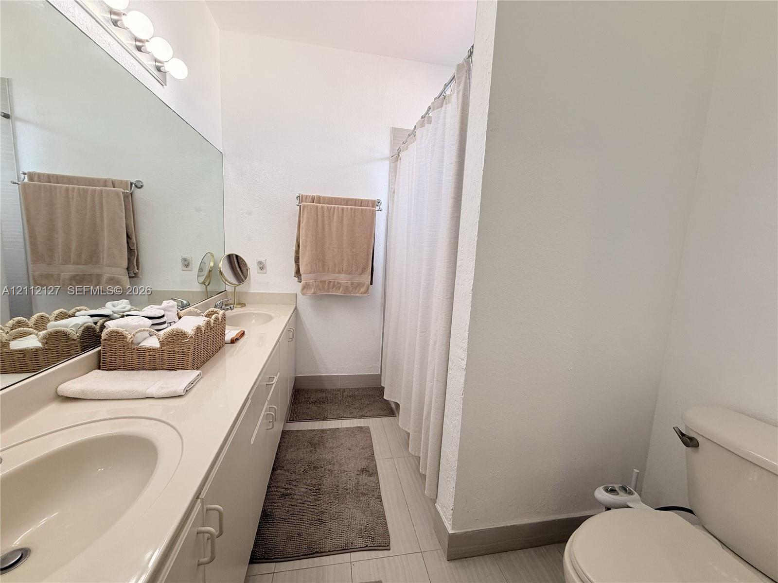 Bathroom featuring an expansive integrated vanity with dual oval sinks, a large wall-mounted mirror, and a tub-shower combination with a shower curtain