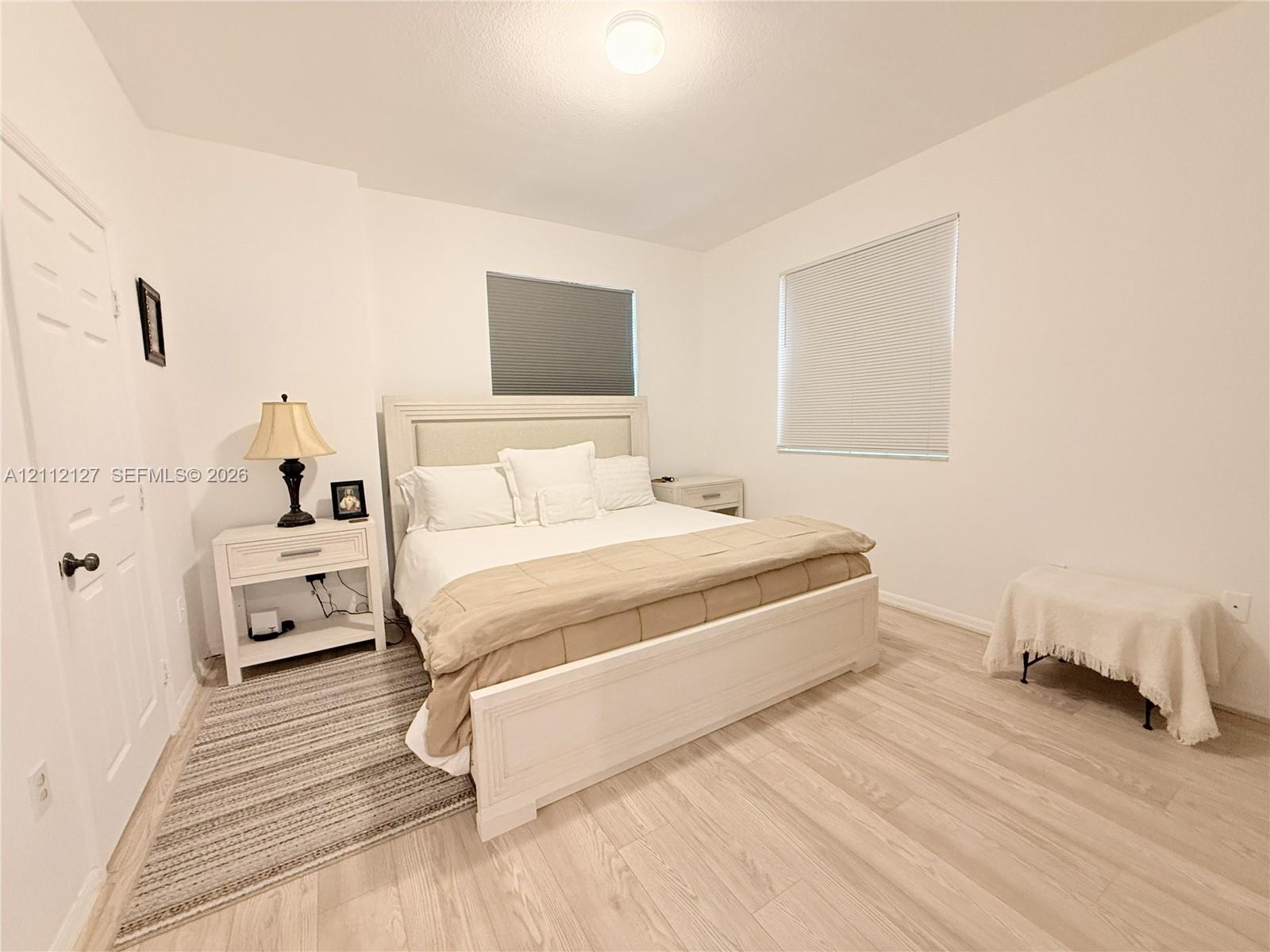 Neutral-toned walls, wood-finish flooring, two windows with fitted shades, and a flush-mount ceiling light fixture
