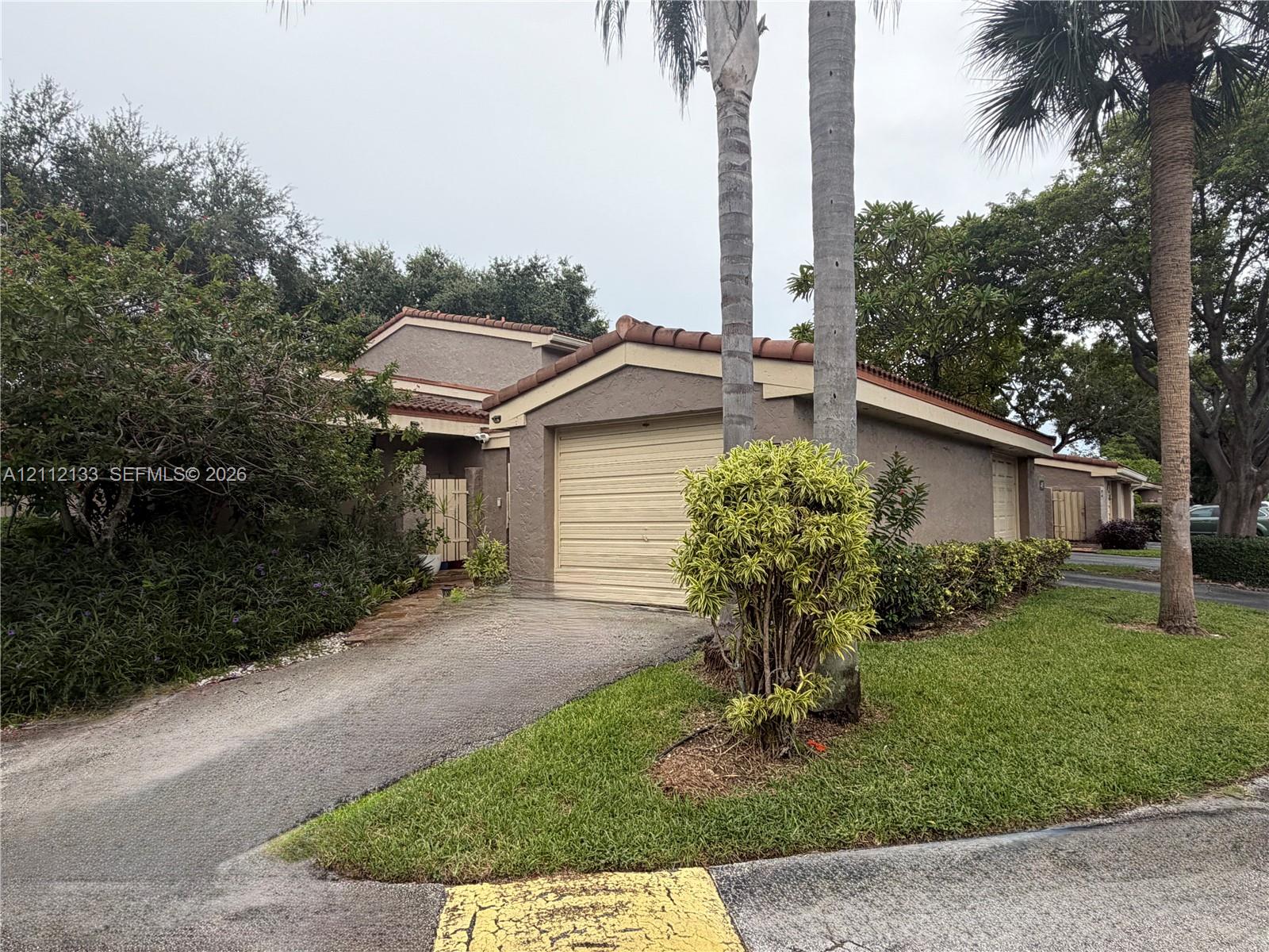 Stucco exterior featuring a tile roof, an attached garage, and mature palm trees within a landscaped front lawn