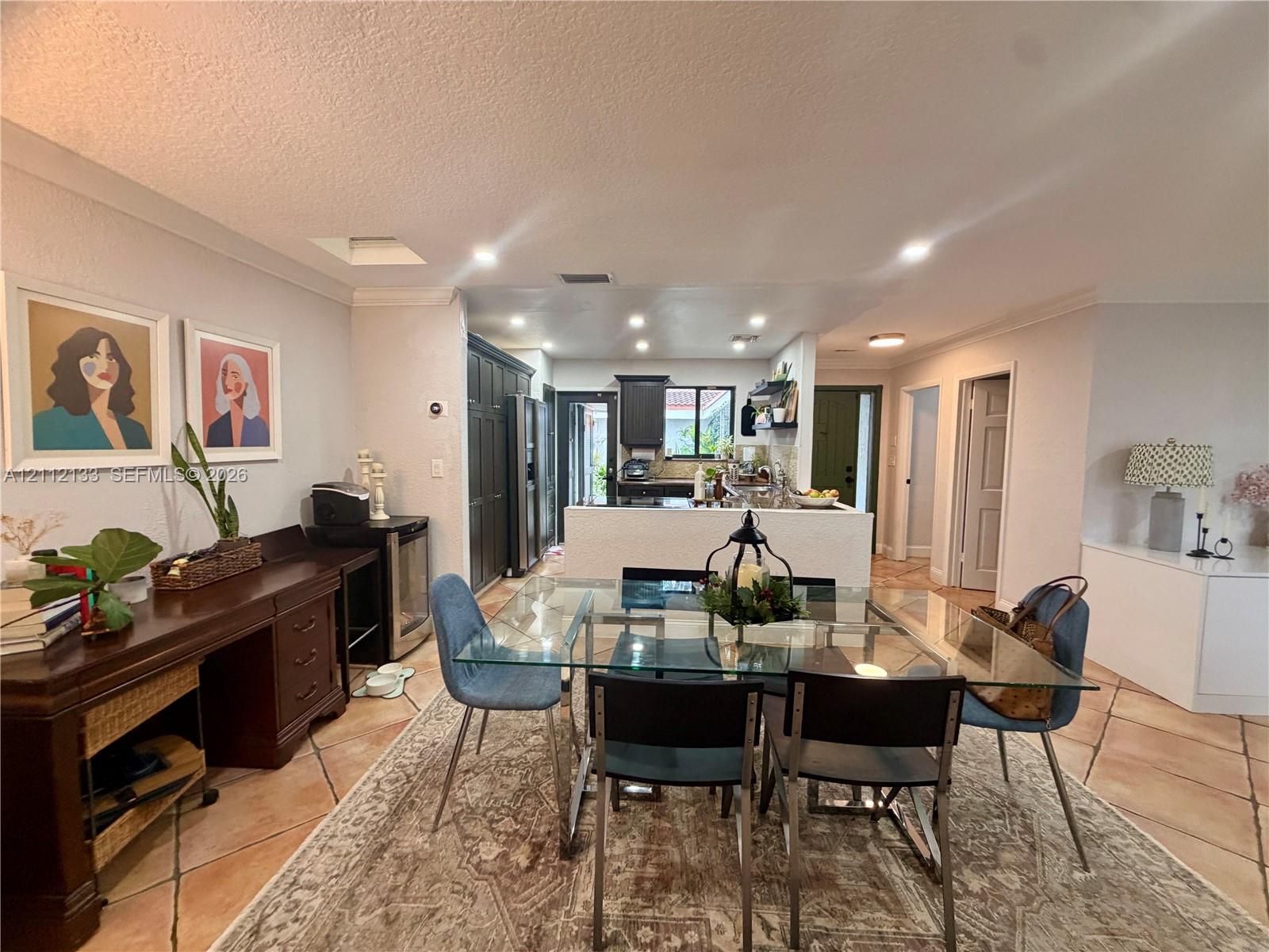 Open-concept kitchen area featuring large-format diagonal tile flooring, recessed ceiling lighting, a white kitchen island, and dark-toned cabinetry