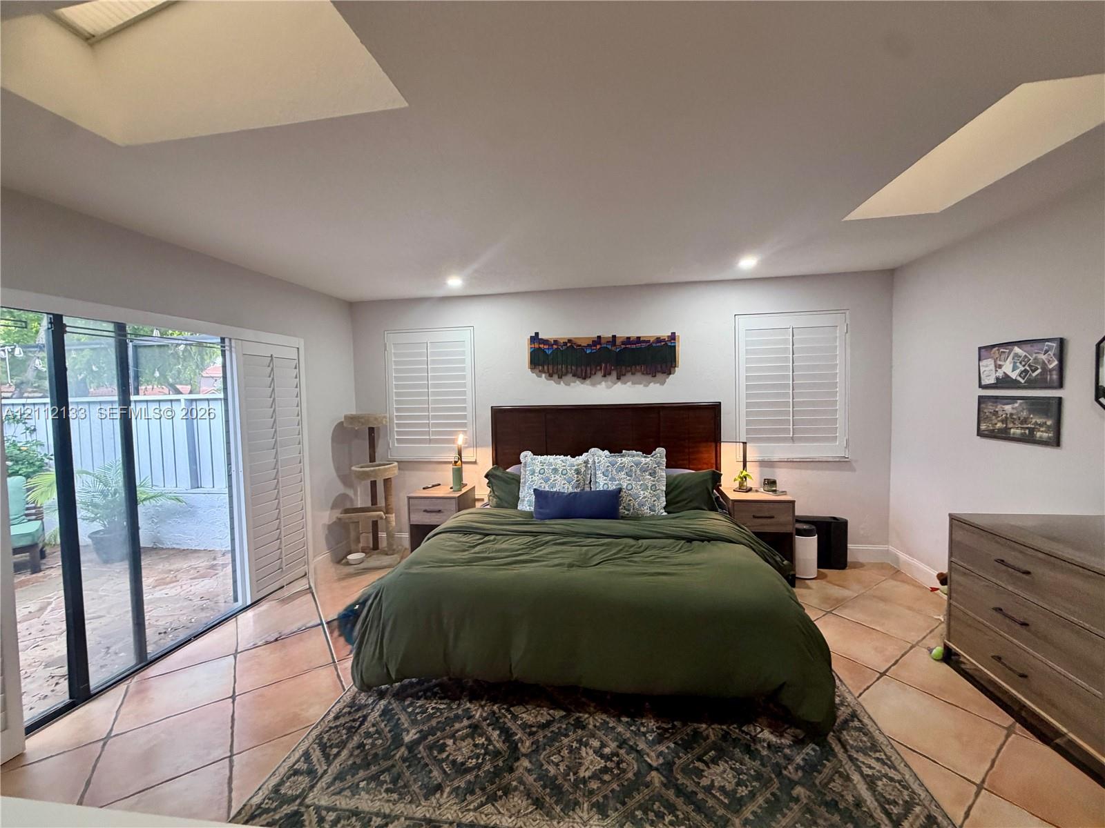 Spacious room featuring vaulted ceilings with dual skylights, large sliding glass doors, tile flooring, and plantation shutters