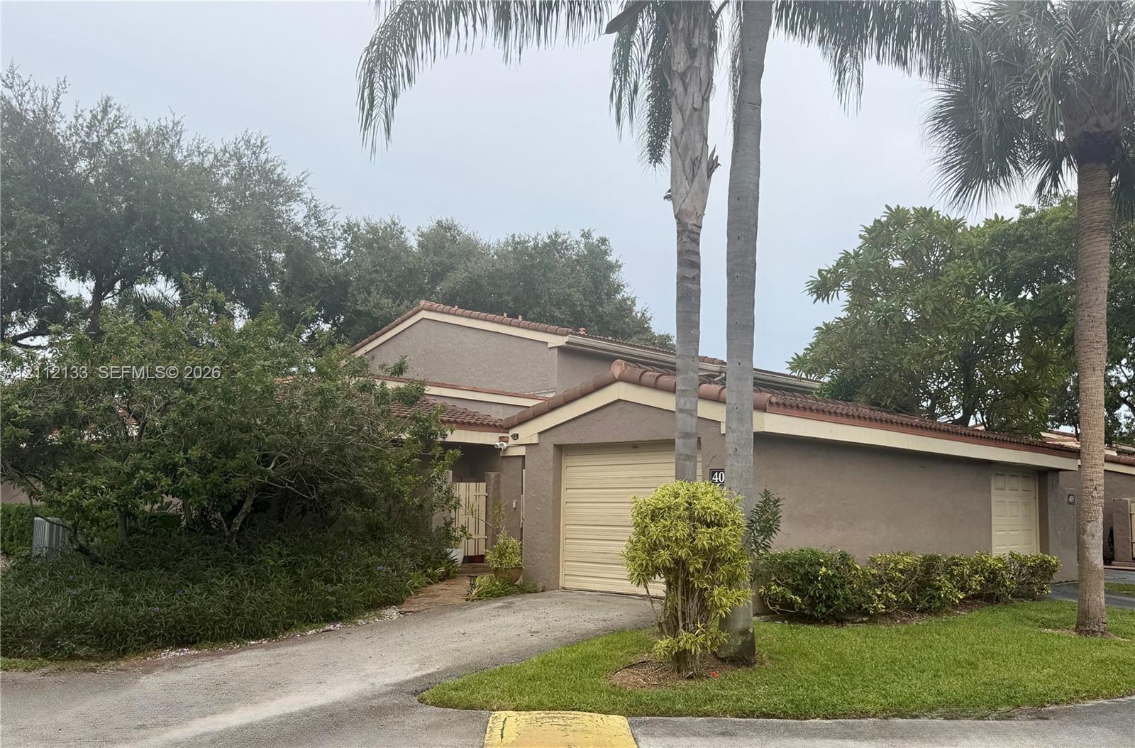 Stucco exterior featuring a dual-garage configuration, a tile roof, and mature palm landscaping