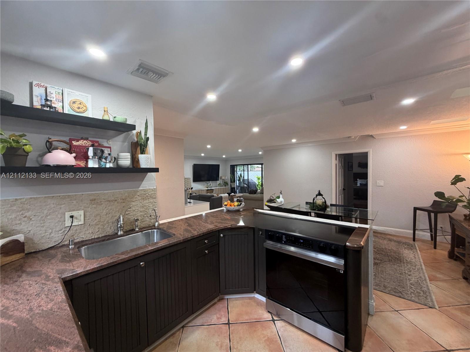 Kitchen featuring dark cabinetry, stone-finish countertops, an undermount stainless steel sink, built-in recessed lighting, and wall-mounted shelving