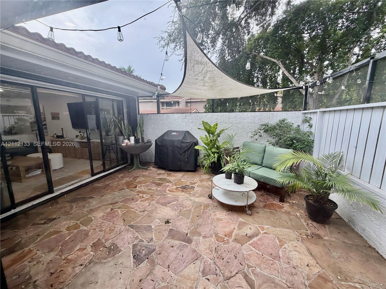 Flagstone patio featuring a white perimeter wall, sliding glass doors, and a suspended triangular shade sail