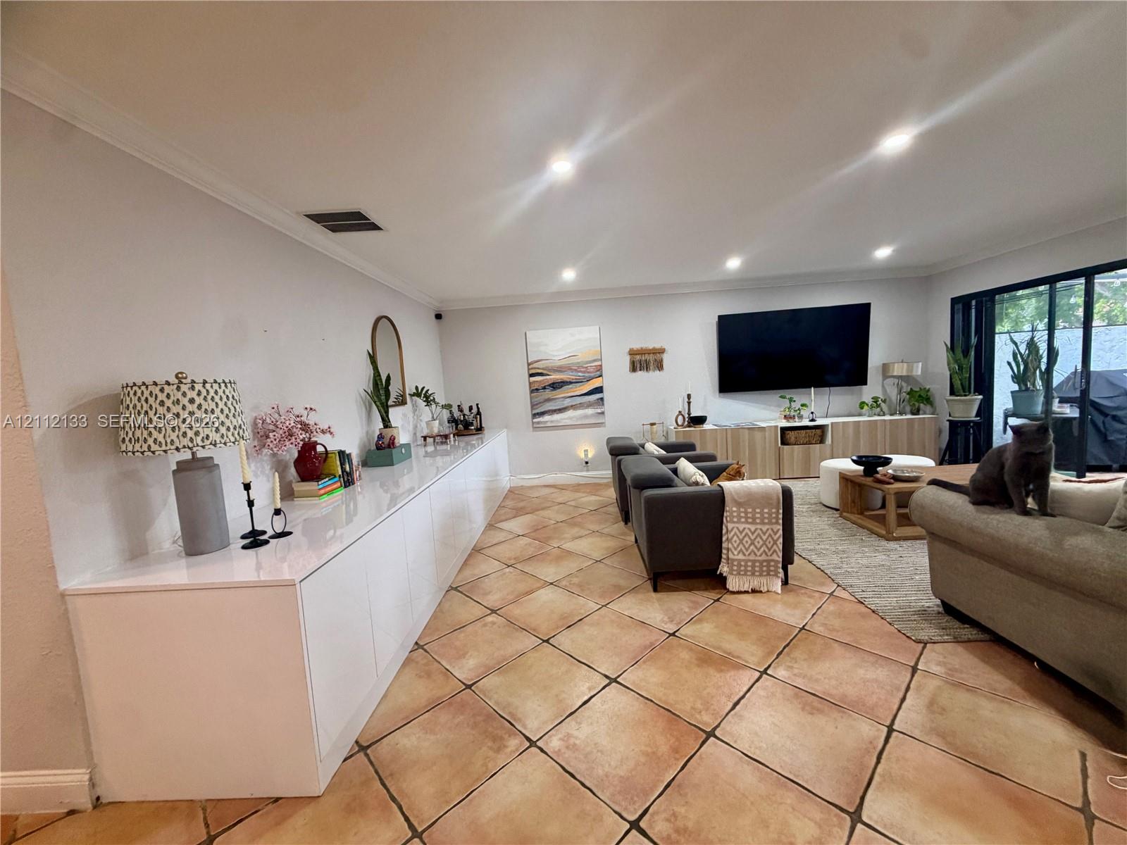 Spacious living area featuring diagonal-set tile flooring, expansive built-in white cabinetry, recessed lighting, and large sliding glass doors