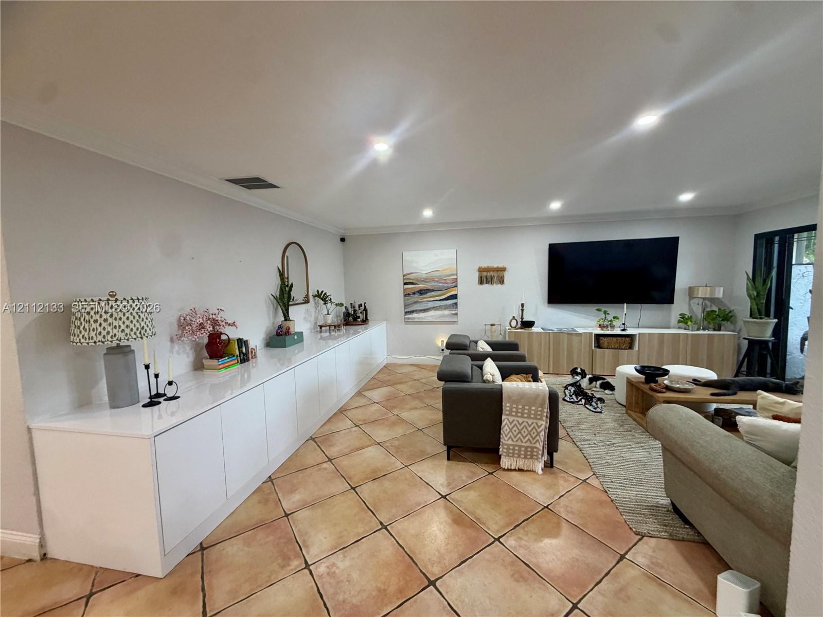 Open-concept interior featuring large-format diagonal tile flooring, extensive built-in white cabinetry with a sleek finish, recessed ceiling lighting, and wood-toned media storage cabinetry