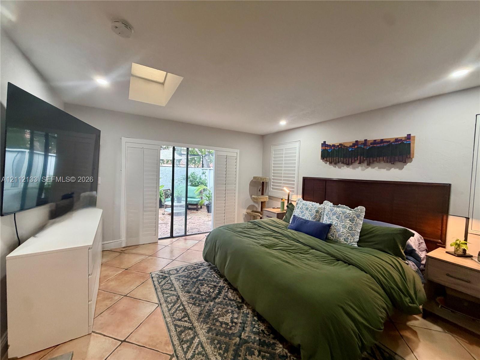 Room featuring tile flooring, a built-in skylight, sliding glass patio doors with white plantation shutters, and recessed lighting