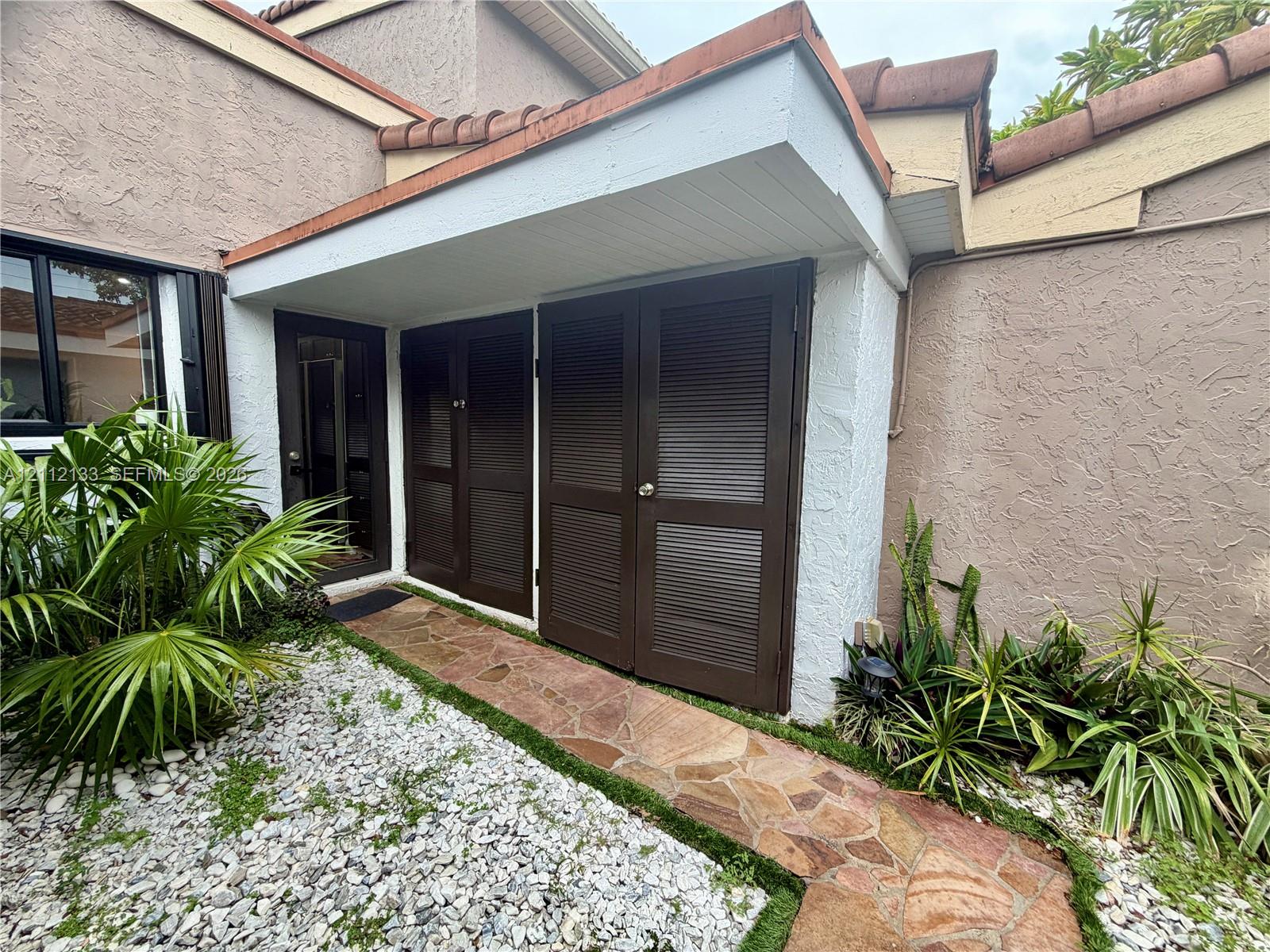 Stucco exterior featuring dual louvered storage doors, flagstone pathway, and a recessed entryway