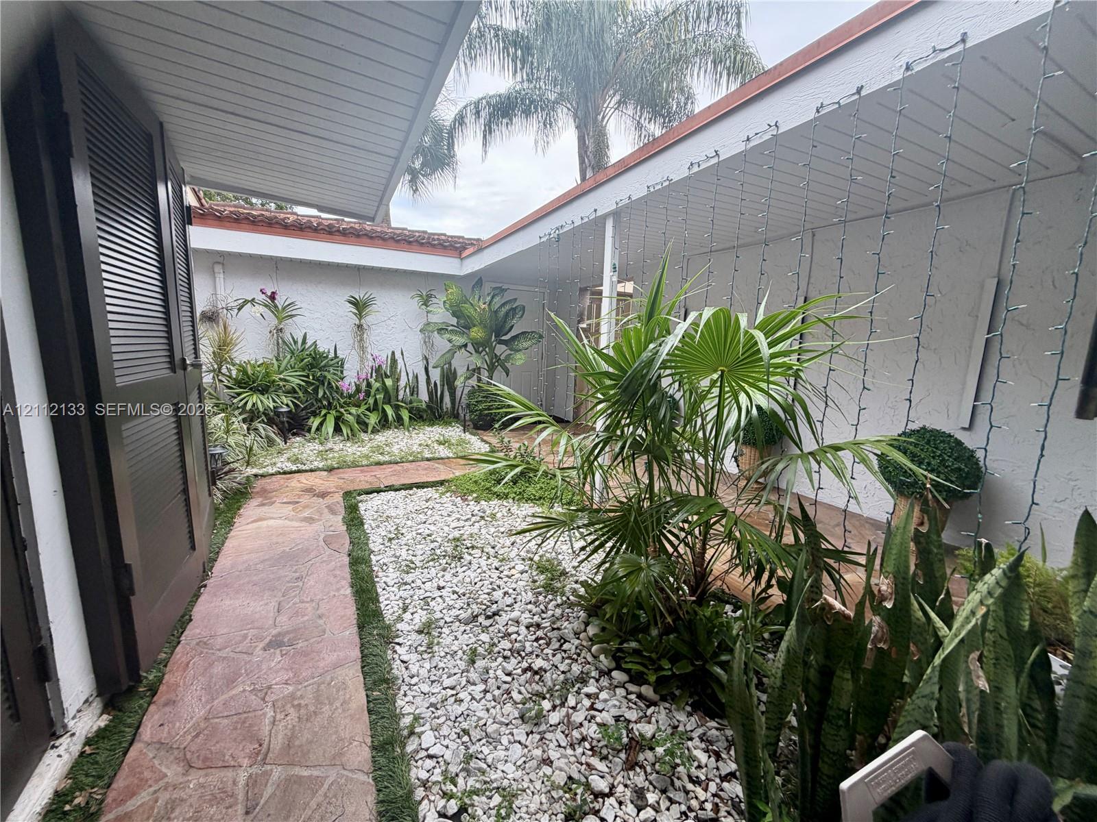 Enclosed courtyard featuring flagstone walkways, white stone ground cover, mature landscaping, and covered perimeter walkways