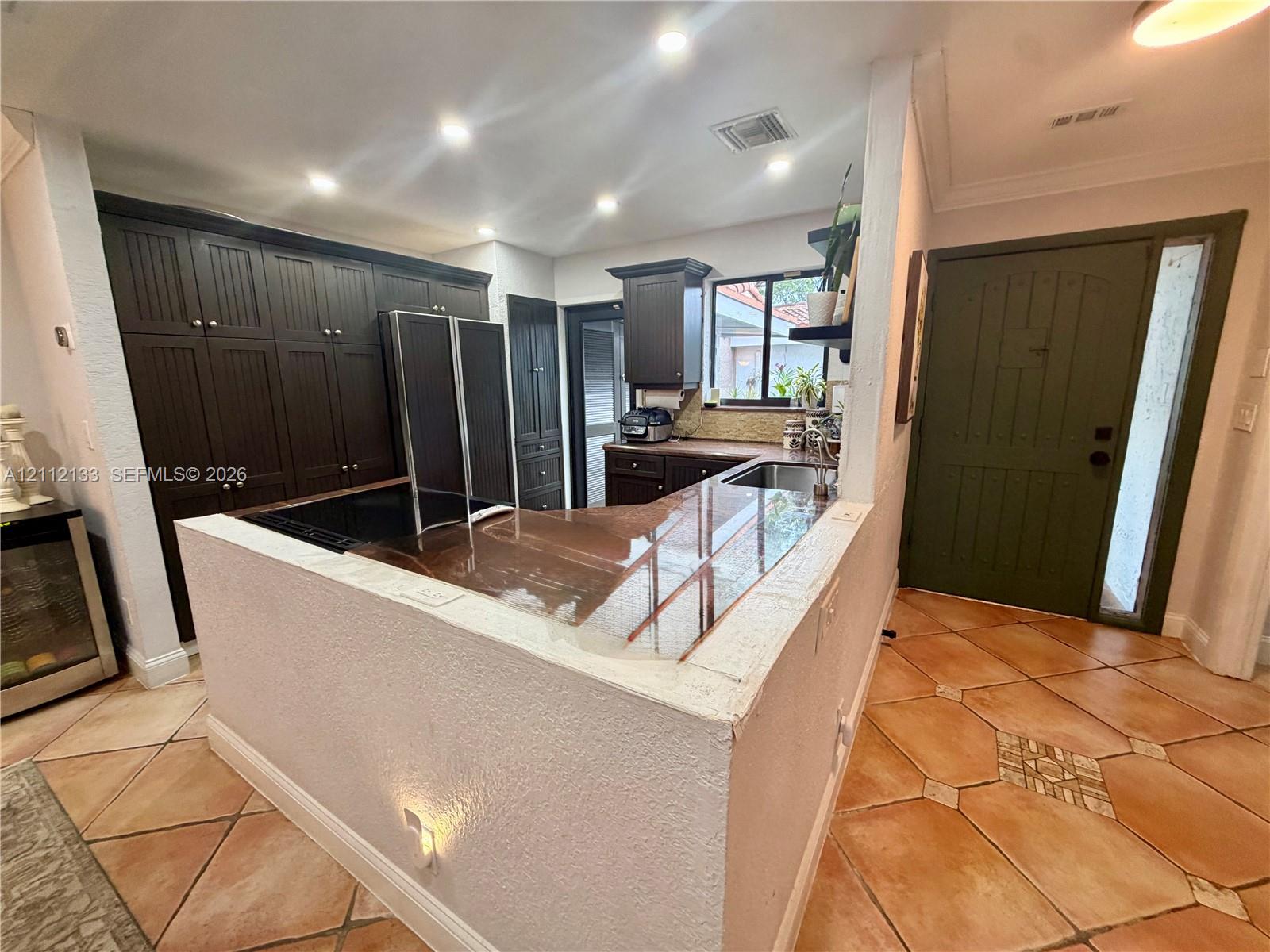 Kitchen featuring dark-finish cabinetry, a wrap-around stone-surface breakfast bar, recessed lighting, and tile flooring
