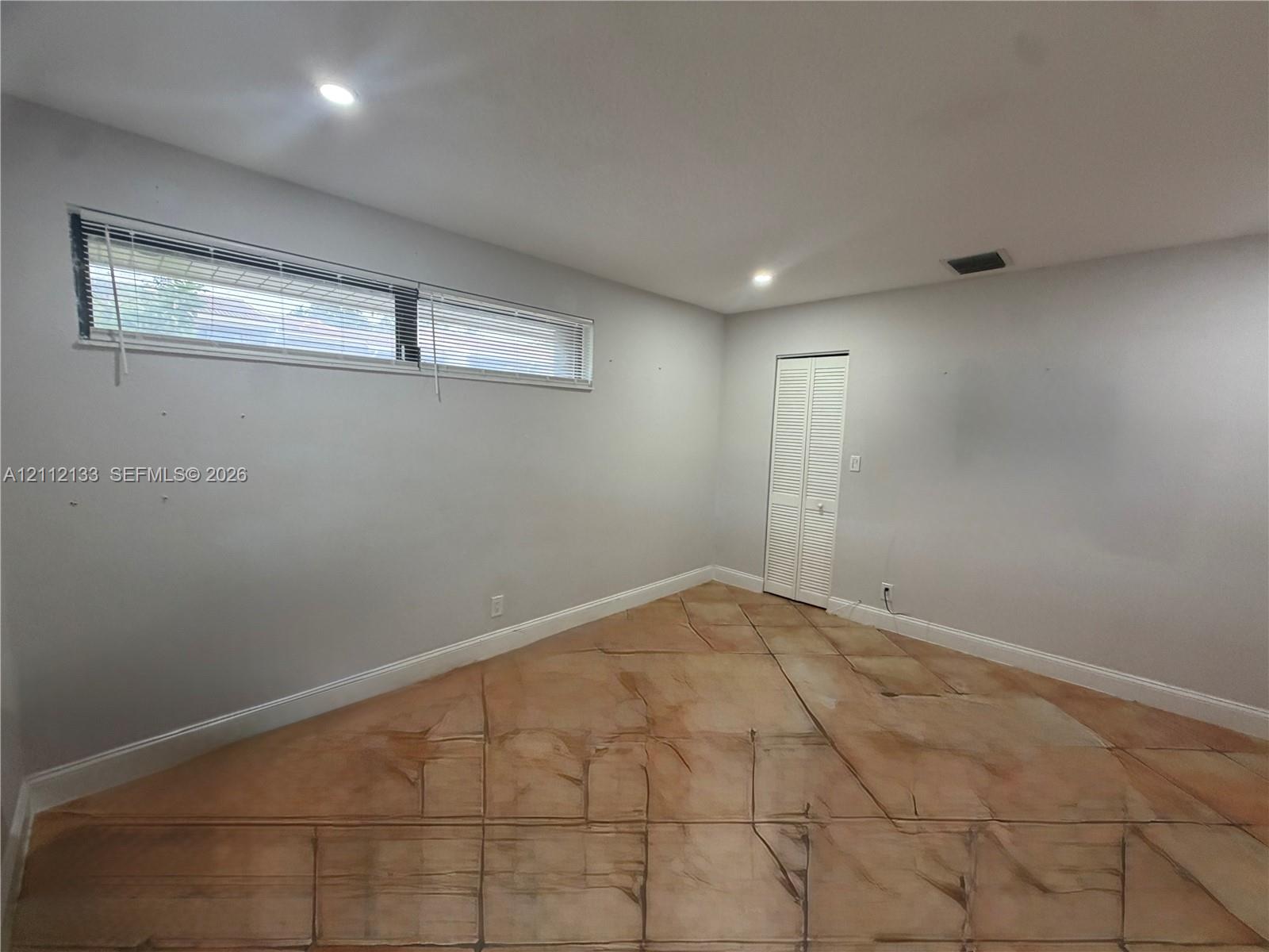 Neutral-toned interior space featuring light-reflective stone-finish tile flooring, recessed ceiling lighting, and a horizontal window with integrated blinds