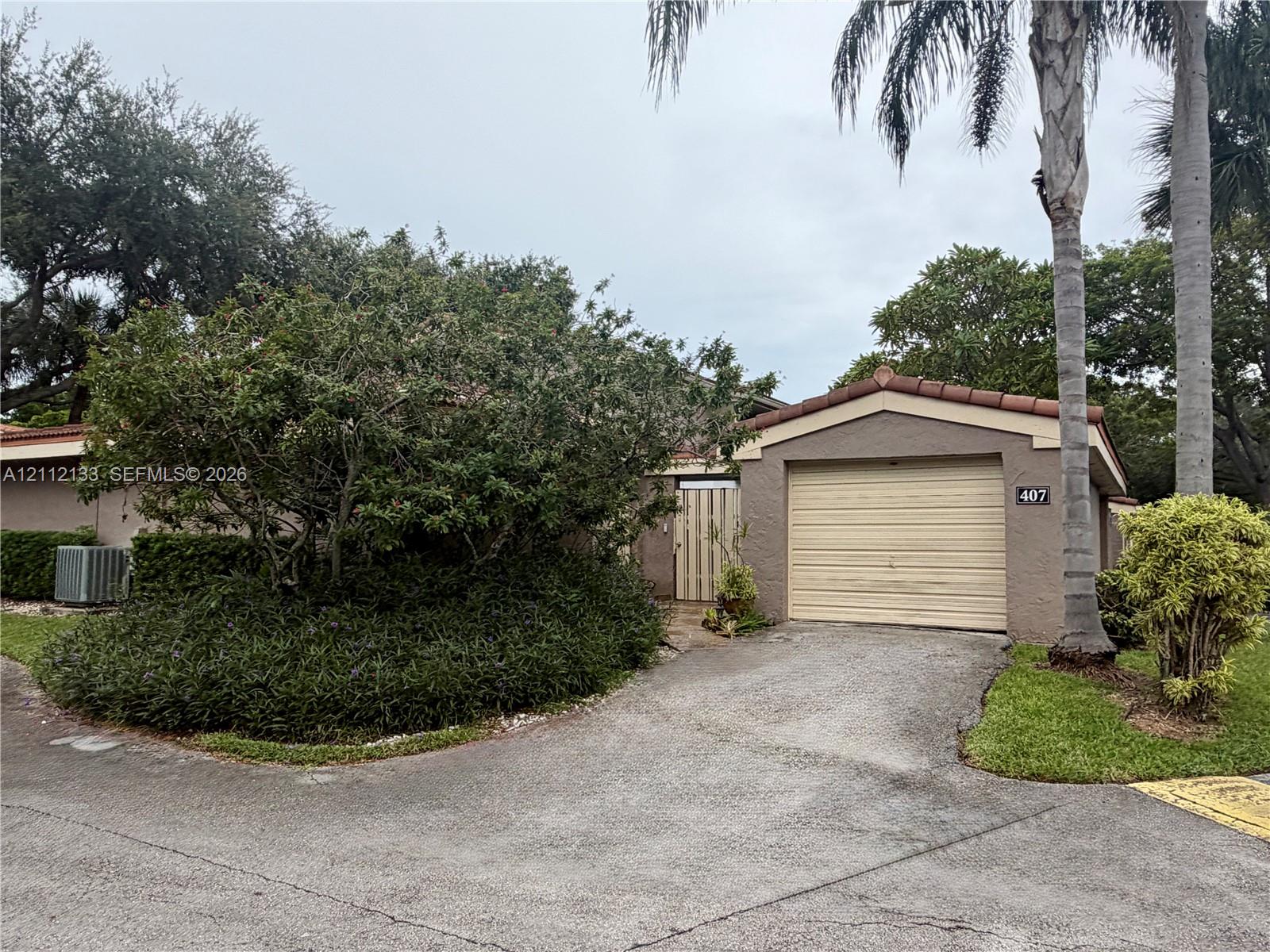 Stucco exterior featuring a tile roof, an attached one-car garage, and established landscaping with mature palm trees