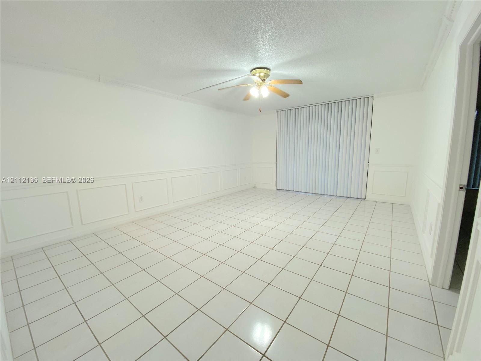 Interior space featuring tile flooring, wall wainscoting, a ceiling fan with light fixture, and vertical window blinds