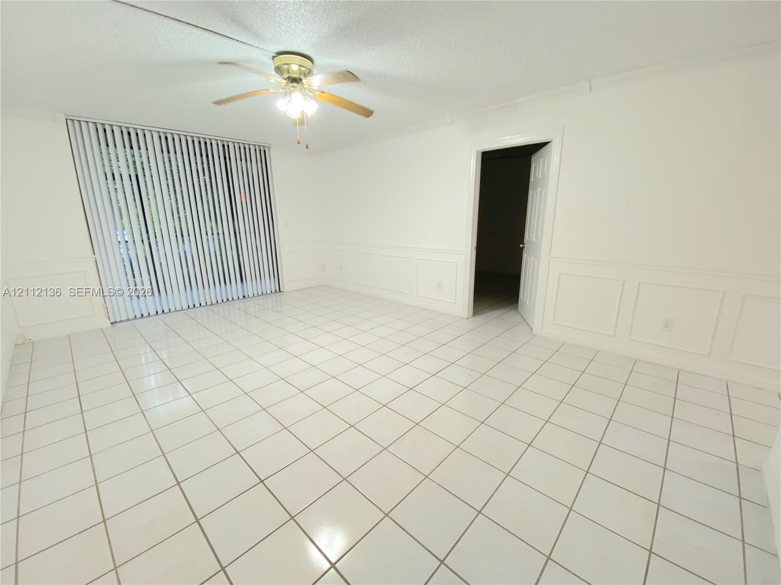 Ceramic tile flooring, white wainscoting, ceiling-mounted light fixture with fan, and vertical window blinds
