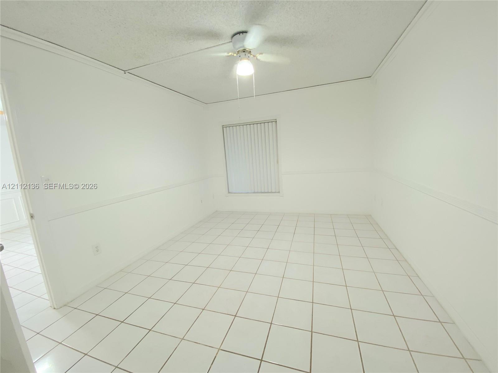 Room featuring light-colored tile flooring, wall-mounted wainscoting, and a ceiling-mounted light fixture with a fan