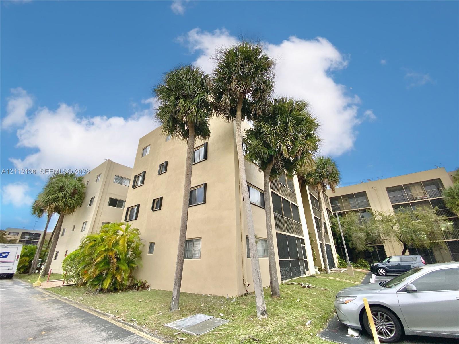 Multi-story stucco exterior featuring screened lanais and mature palm trees