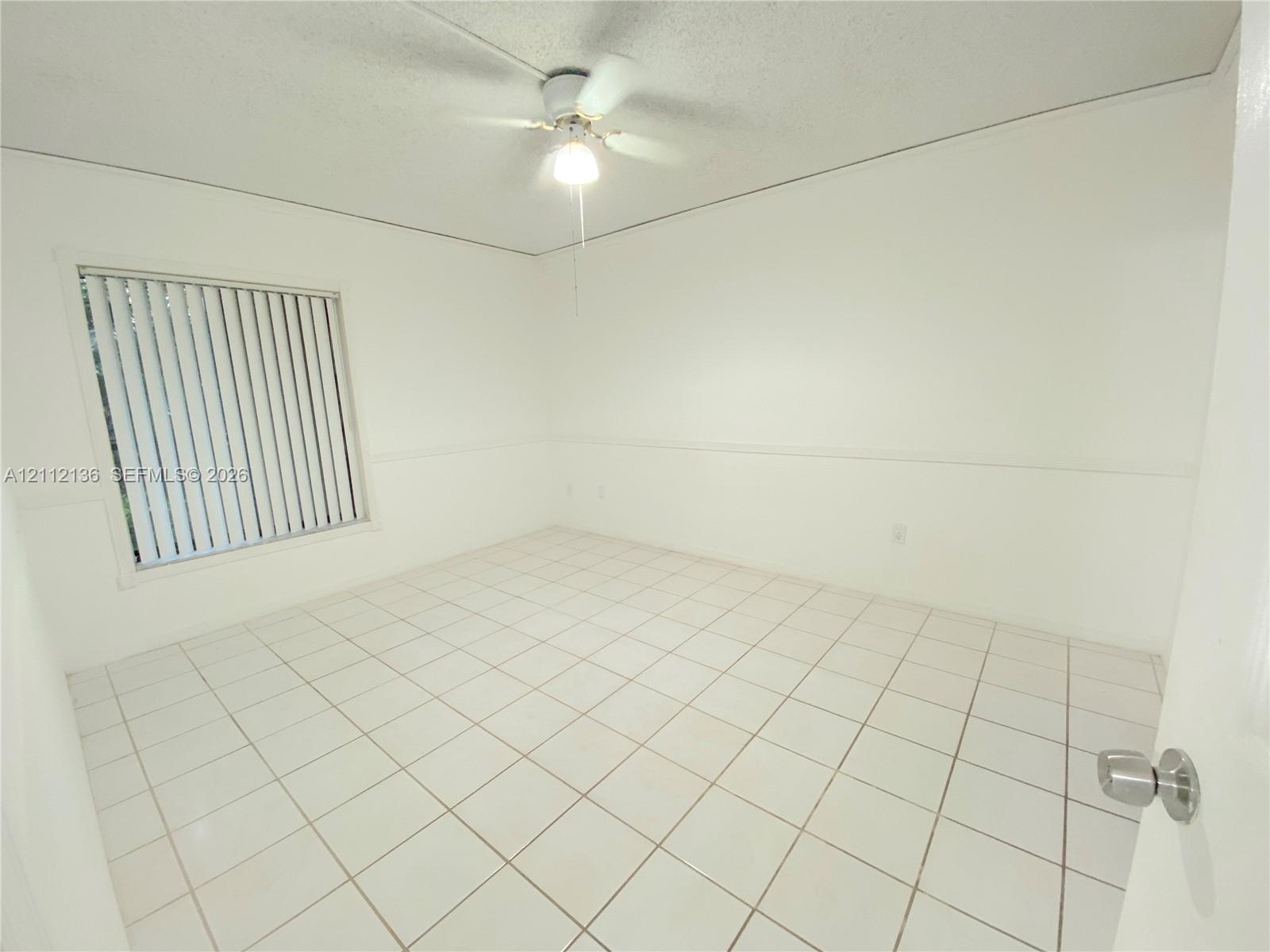 Neutral-toned room featuring large-format square tile flooring, white chair rail molding, vertical window blinds, and a central ceiling fan with an integrated light fixture