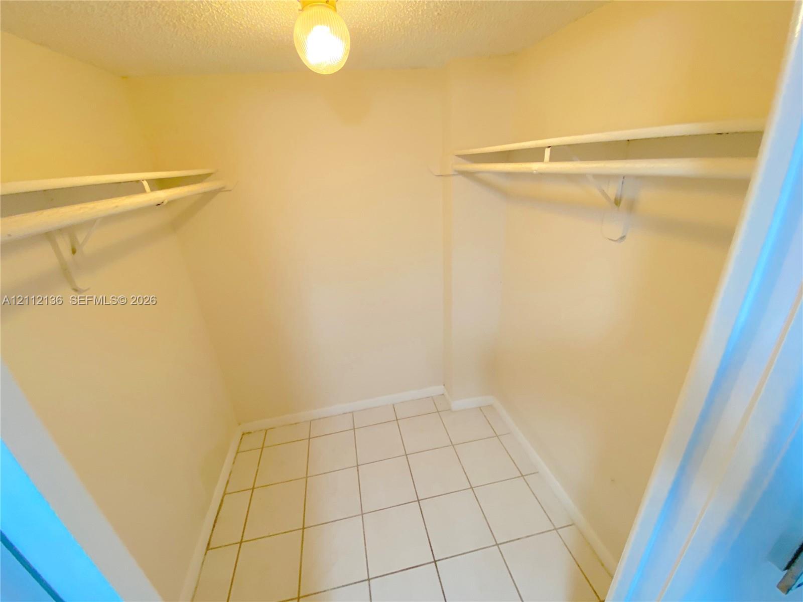 Walk-in storage space featuring ceramic tile flooring, dual-level wall-mounted shelving, and a central ceiling light fixture