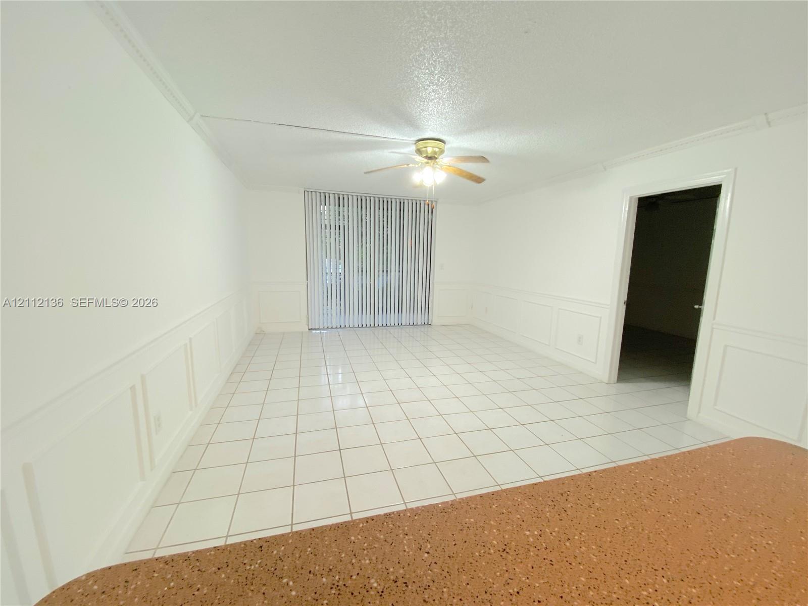 Interior area featuring white tile flooring, white wainscoting, a ceiling fan with integrated lighting, and sliding glass doors with vertical blinds