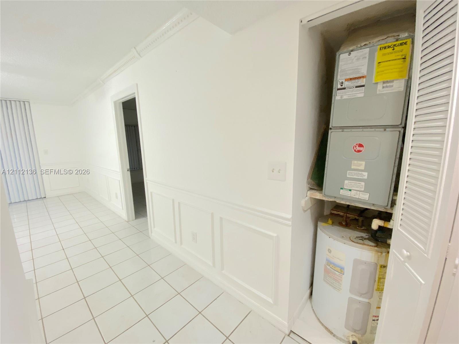 Interior space featuring white tile flooring, detailed wall wainscoting, crown molding, and a louvered-door utility closet housing the HVAC unit and water heater