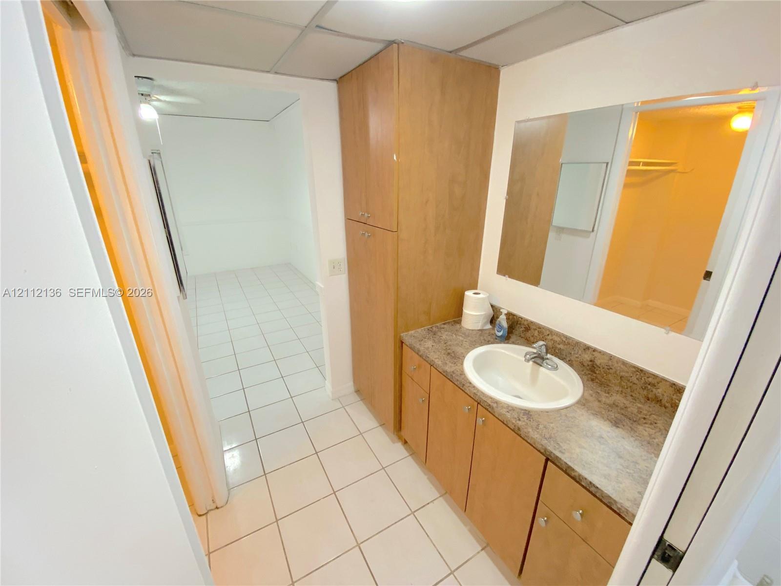 Vanity featuring wood-finish cabinetry, a full-height storage cabinet, a solid-surface countertop, and a recessed oval sink