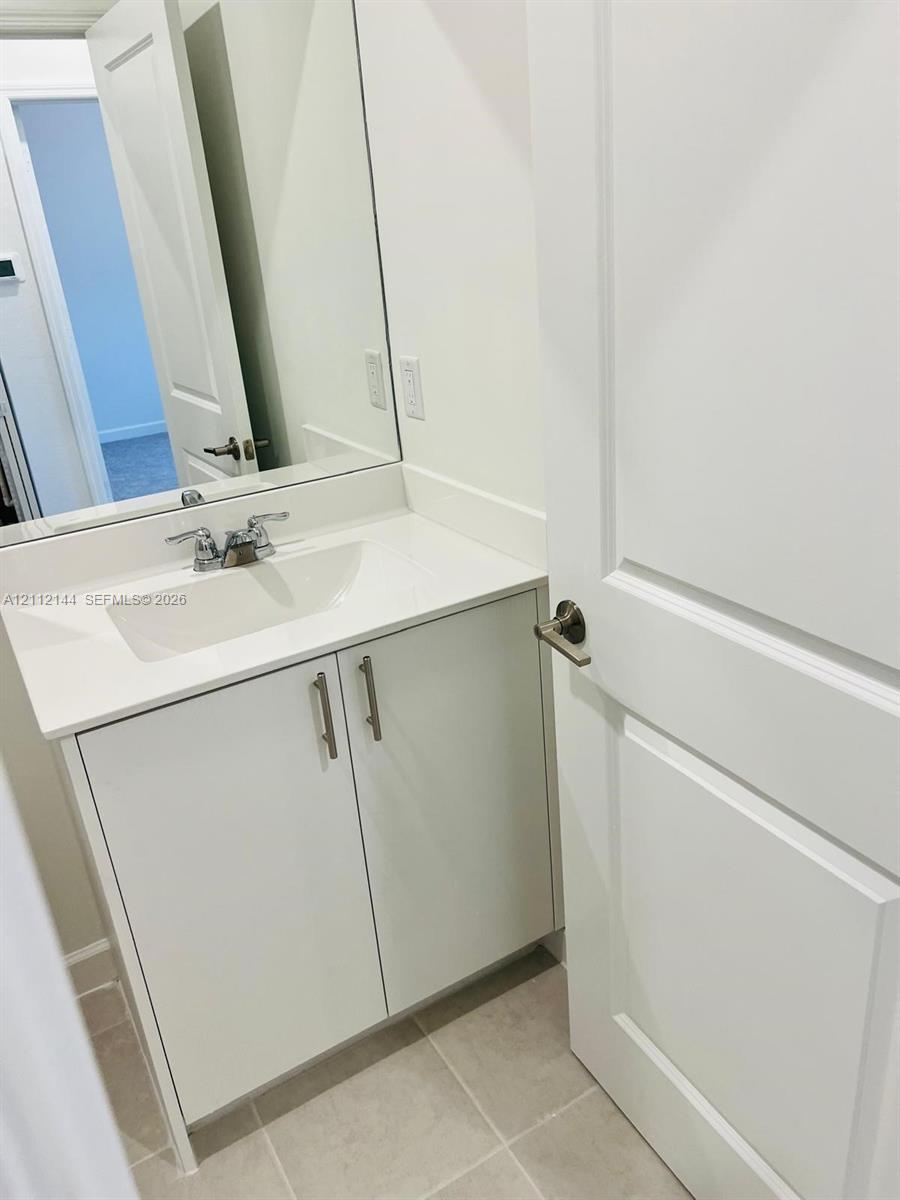 Bathroom vanity featuring a solid-surface countertop, an integrated sink, polished chrome faucet, white cabinetry with brushed nickel pulls, and a wall-mounted mirror