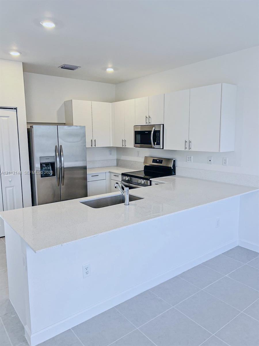 Kitchen featuring white cabinetry, solid-surface countertops, a stainless steel refrigerator, a built-in microwave, and tile flooring