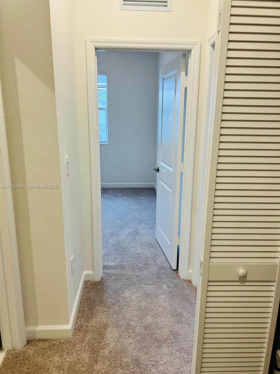 Interior space featuring neutral-toned carpeting, a multi-panel door, and white louvered closet doors