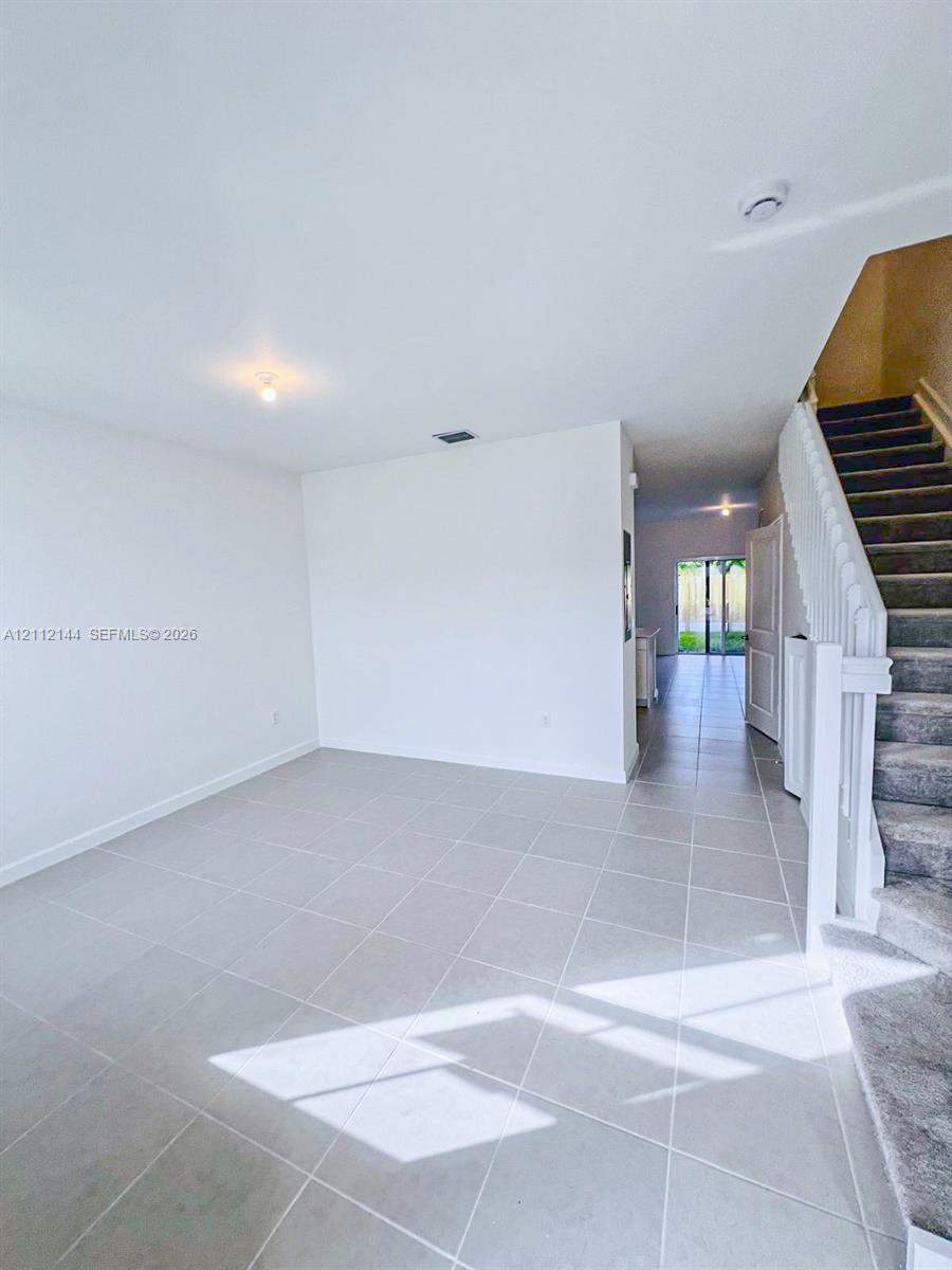 Neutral-toned tile flooring, white wall finishes, and a staircase featuring carpeted steps with a white balustrade