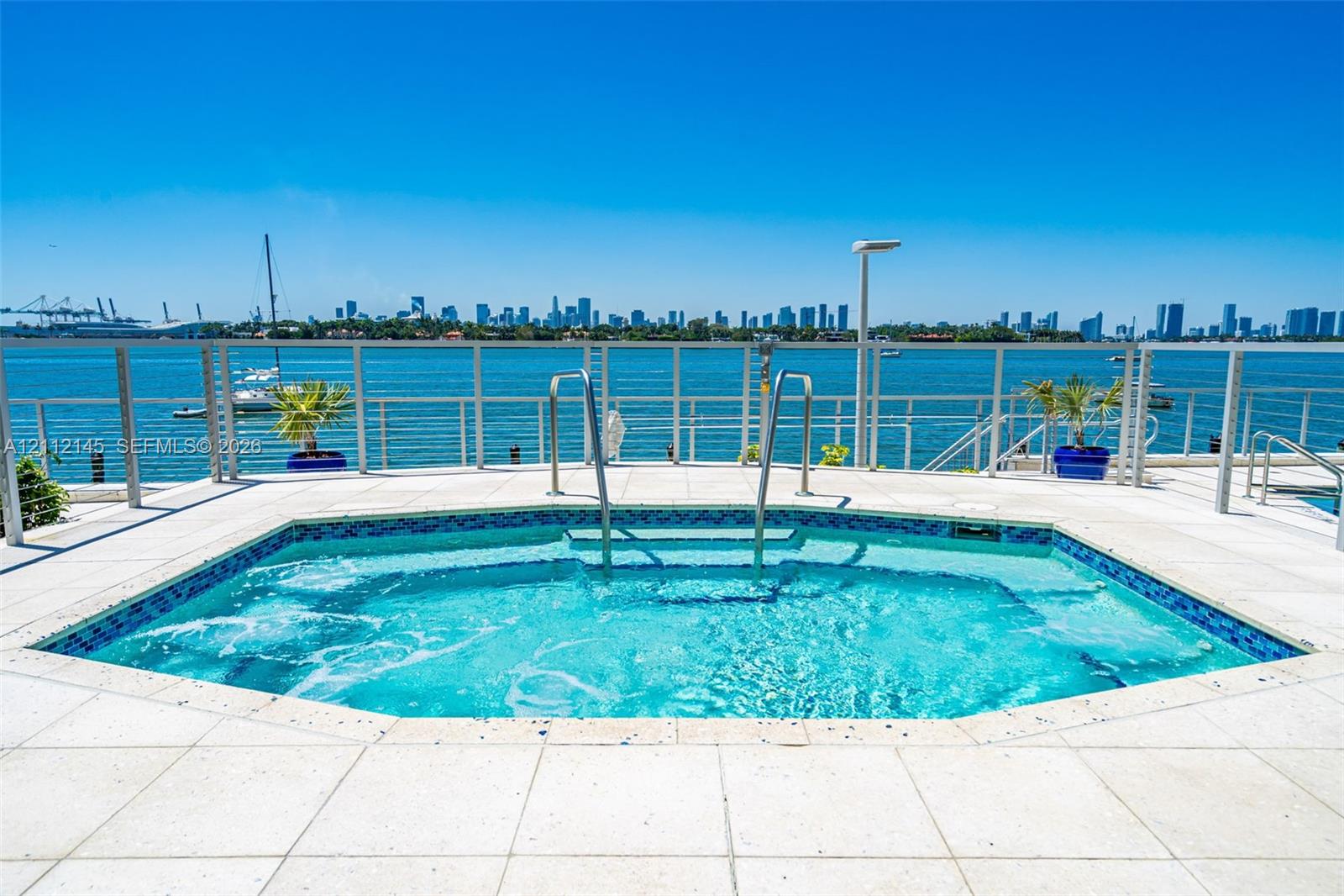 In-ground spa with tile detailing, surrounded by paved stone decking, stainless steel handrails, and a metal perimeter railing In-ground spa with tile detailing, surrounded by paved stone decking, stainless steel handrails, and a metal perimeter railing