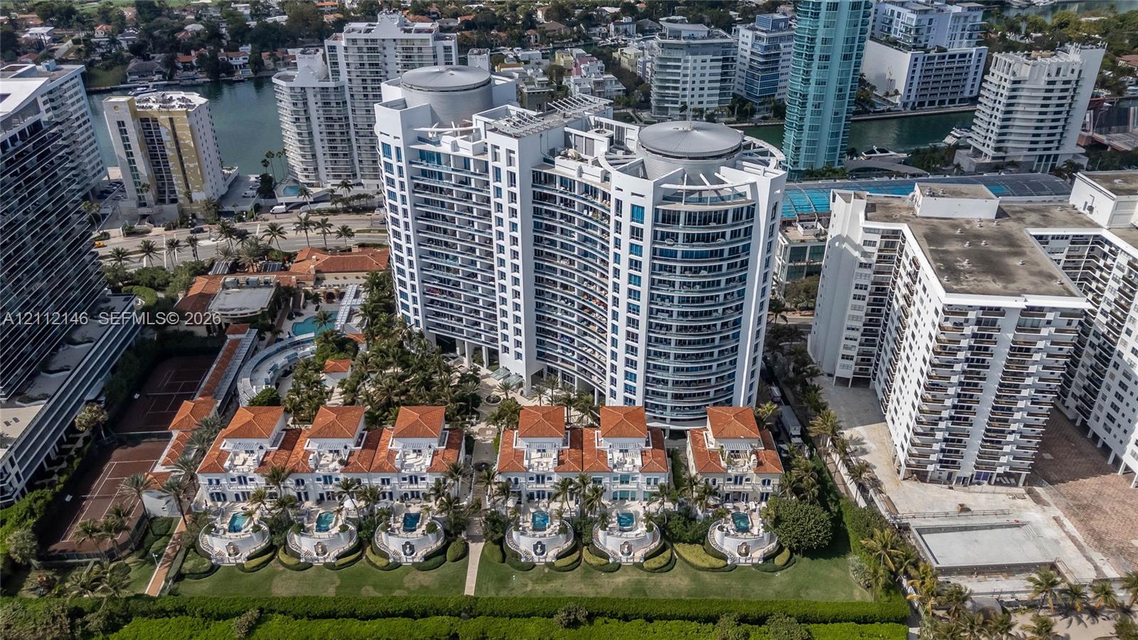 Aerial perspective of a high-rise residential complex featuring a tiered building design, terra-cotta roof tiles, private ground-level patio pools, and tennis courts
