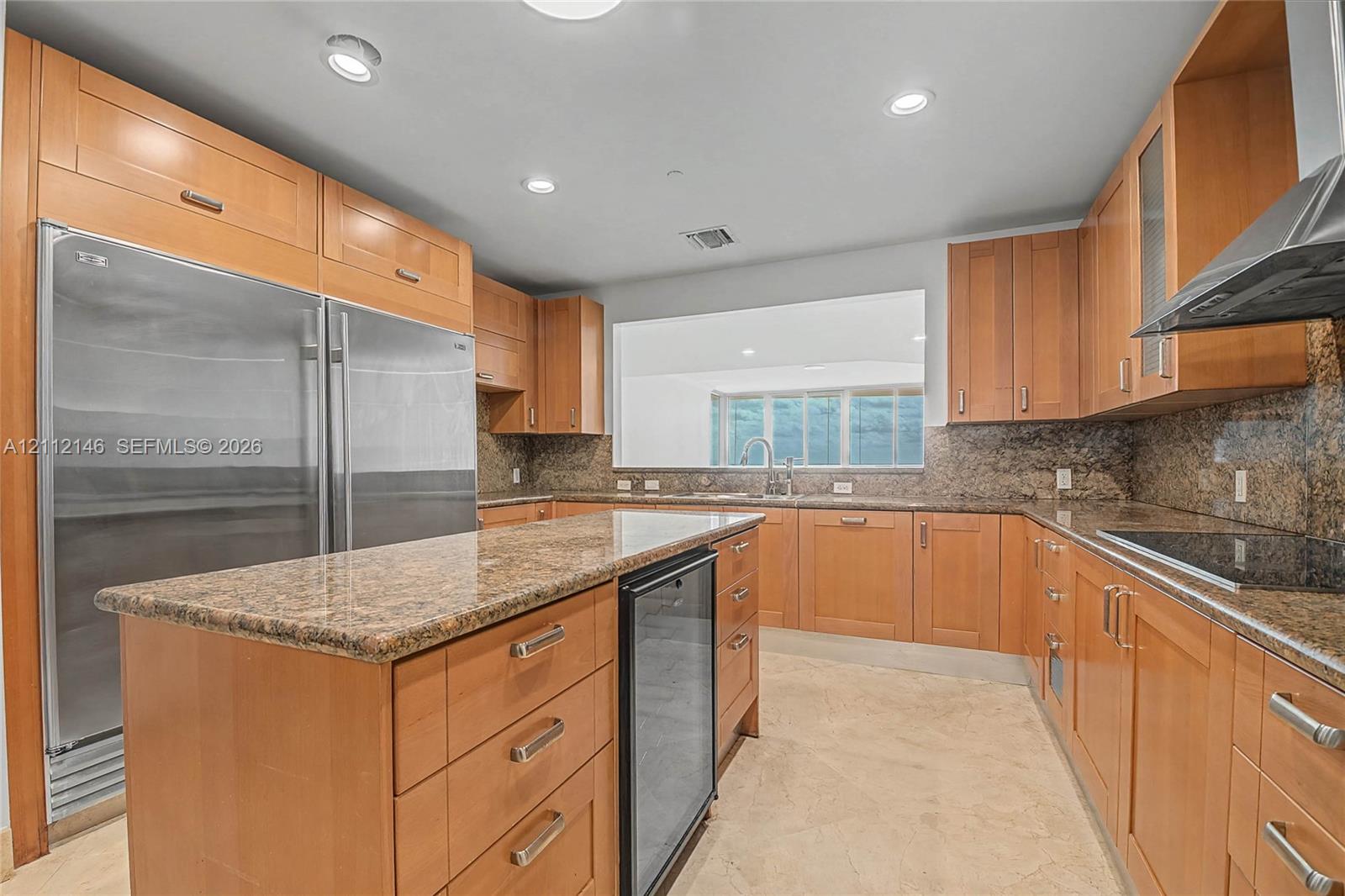 Kitchen featuring wood cabinetry, stone countertops, stainless steel full-size refrigerator, integrated beverage refrigerator, and stainless steel range hood