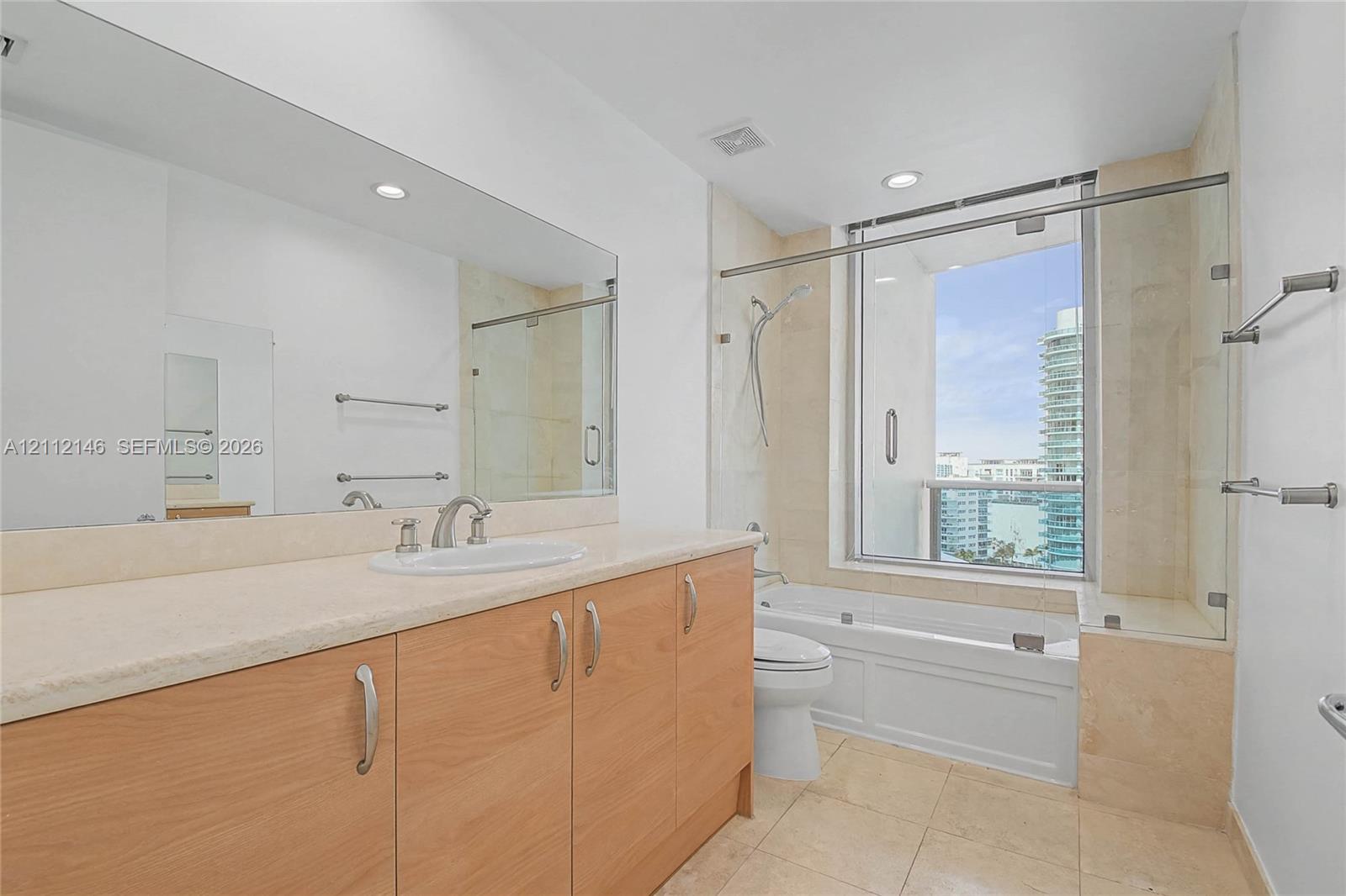 Bathroom featuring a light wood-finish vanity, stone-surfaced countertop, oversized wall mirror, tile flooring, and a combined tub and shower enclosure