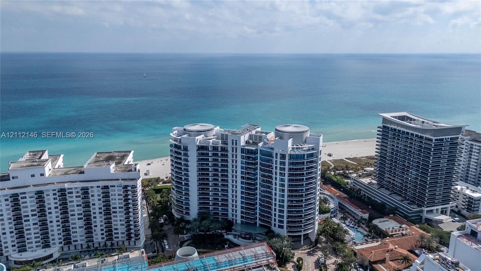 High-rise residential building featuring expansive floor-to-ceiling windows, wrap-around balconies, and direct proximity to the coastline and sandy beach