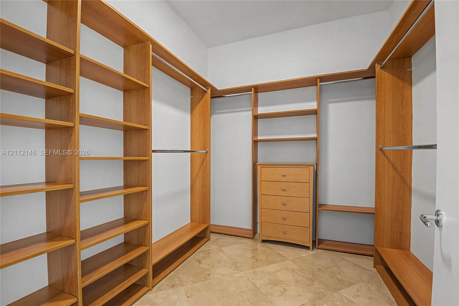 Walk-in closet featuring extensive custom wood-finish shelving, integrated hanging rods, a built-in five-drawer dresser, and stone-tile flooring