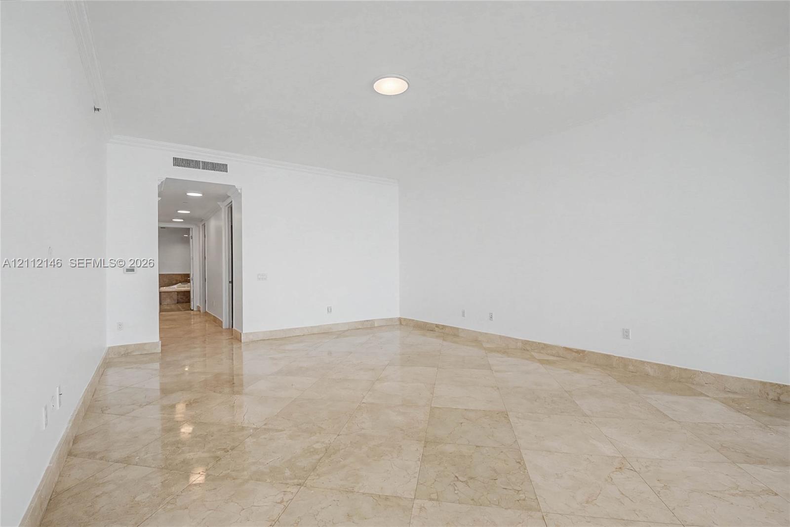 Spacious interior featuring large-format stone flooring laid in a diamond pattern, crisp white wall finishes, crown molding, and recessed ceiling lighting